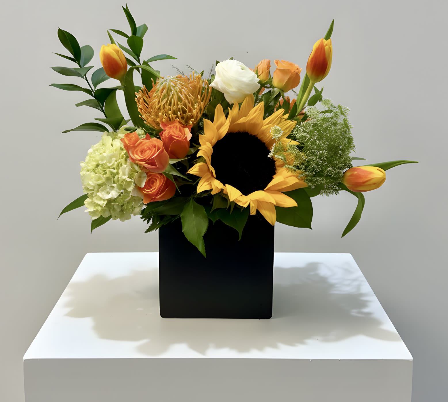 Summer Radiance - A vibrant, cheerful arrangement featuring a bold sunflower, fresh tulips, delicate ranunculus, and lush hydrangea accented with complementary seasonal blooms. Designed with natural movement and texture, it brings a bright, uplifting presence—perfect for any occasion.