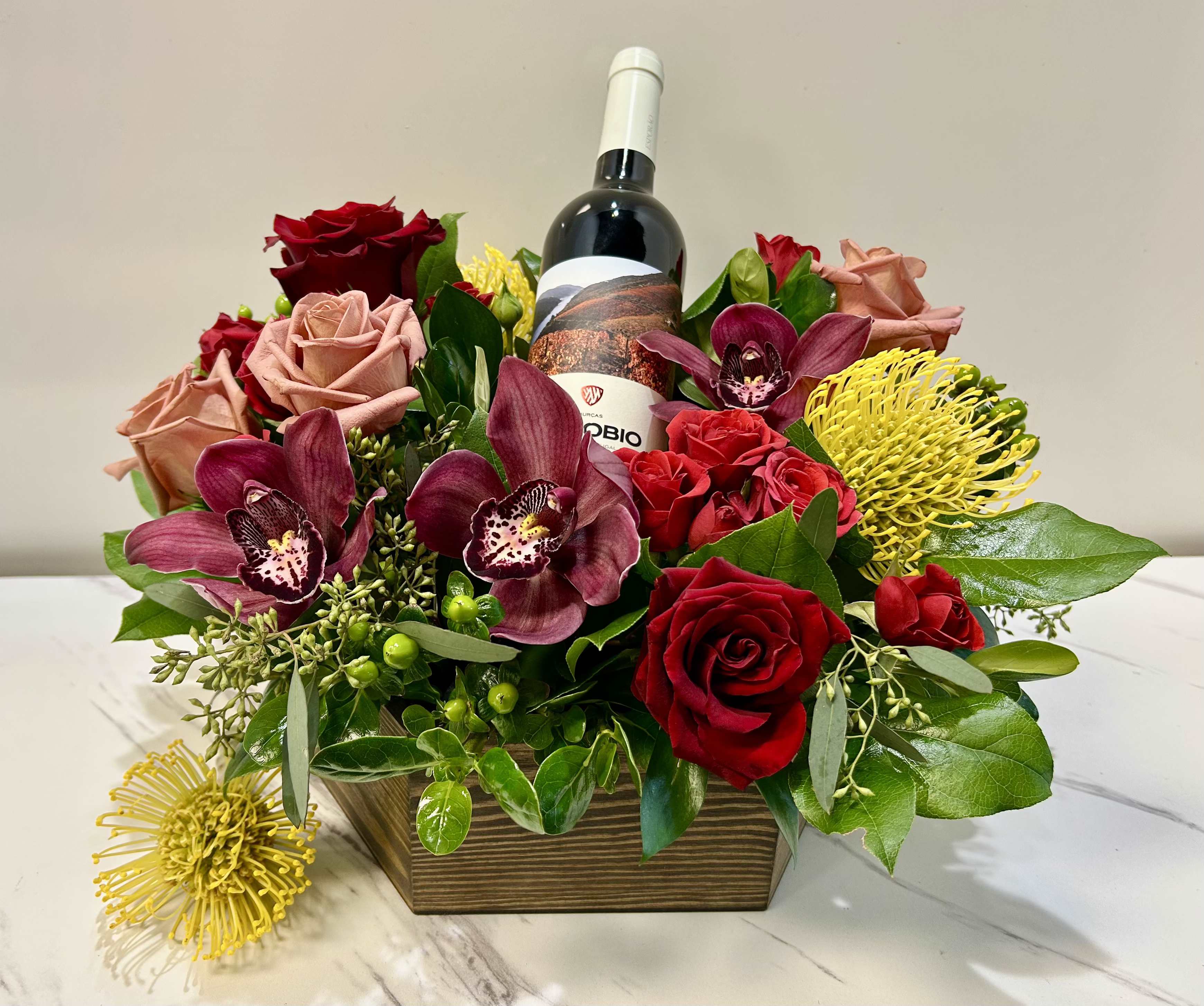 Floral arrangement with roses, orchids, and a wine bottle in a wooden box