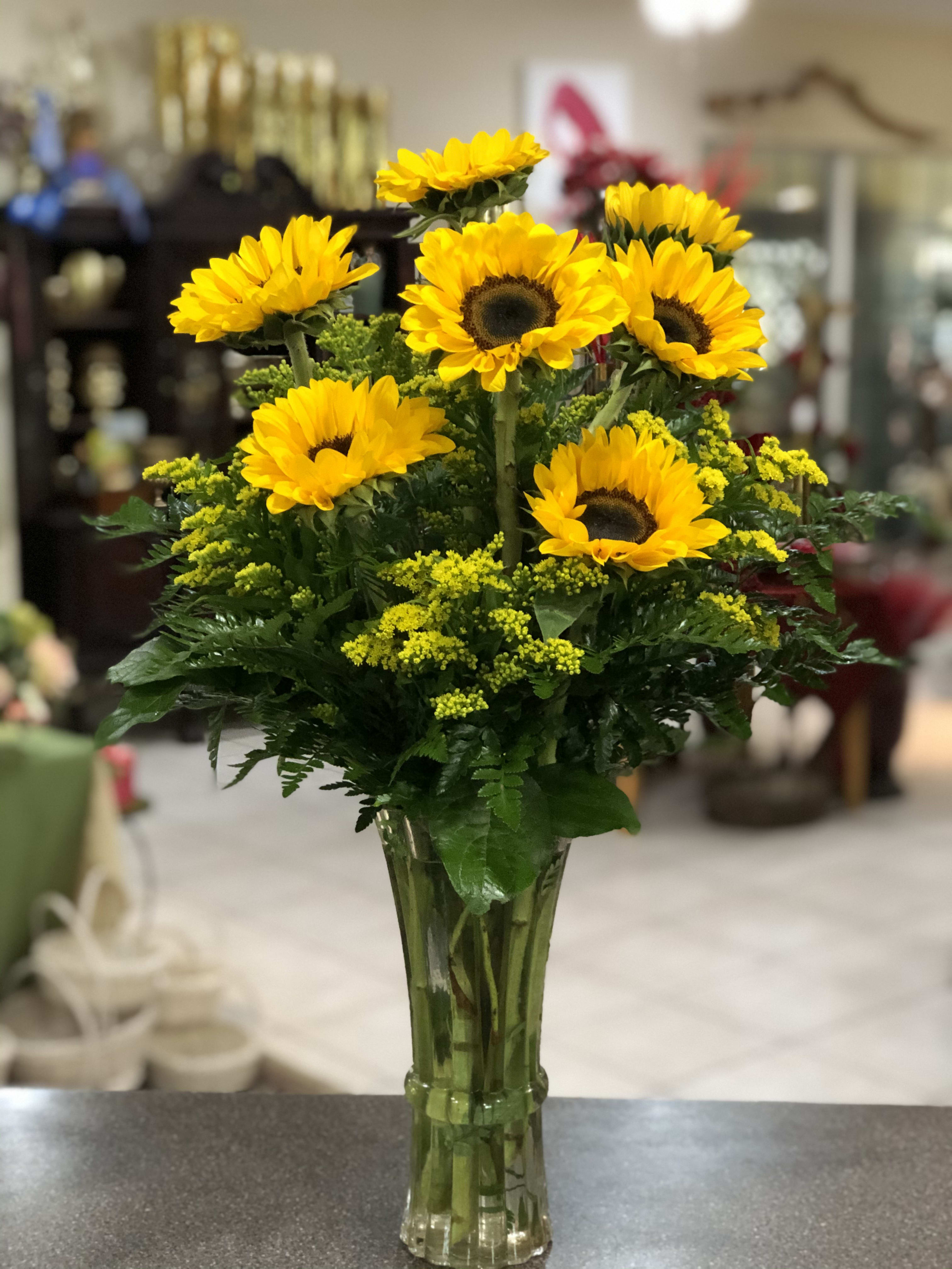 Tall clear vase of yellow sunflowers with small yellow filler flowers