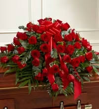 Florist Choice Red Rose Casket Spray - A rich, classical display of love and remembrance, this red rose casket spray places dozens of deep red roses in a dense, arching layer across the top of a wooden casket-an unmistakable sympathy arrangement for funerals and memorial services. The massed roses create a saturated field of color that reads as both solemn and deeply affectionate, making the person you're honoring feel profoundly remembered.  Bright red satin ribbon and a large red bow anchor the center, with trailing streamers that add a formal, dignified finish. The spray's generous coverage provides a striking visual from the front and sides of the casket; designed to lay gracefully across the lid, it pairs classic rose texture and green foliage for contrast. For ordering, specify any service details and we'll ensure timely delivery and respectful placement to reflect your sentiment.  comes in three sizes standard 50 roses , Deluxe 75 roses , premium 100 roses