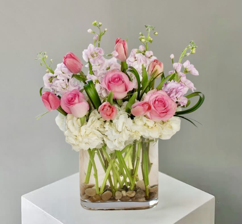 Pink roses and tulips with white hydrangeas in a clear square glass vase with stones