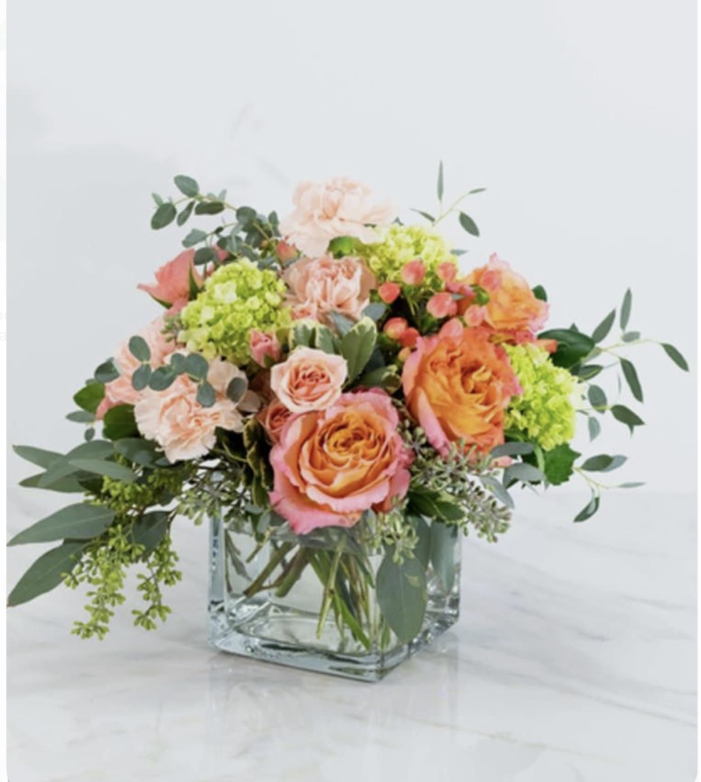 Peach and orange roses with green hydrangeas in a square glass vase