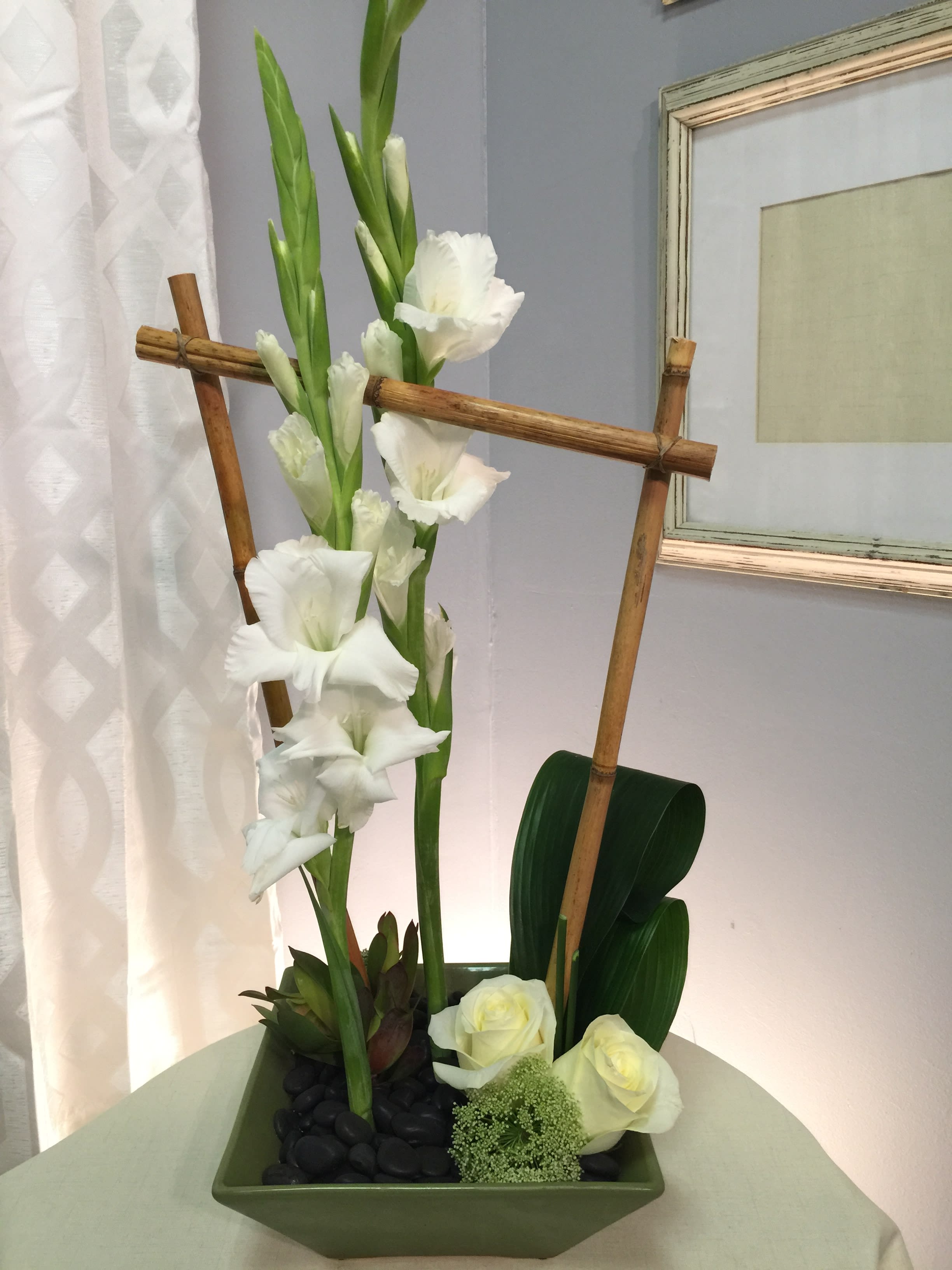 Tall white gladiolus arrangement in a green square vase with bamboo accents