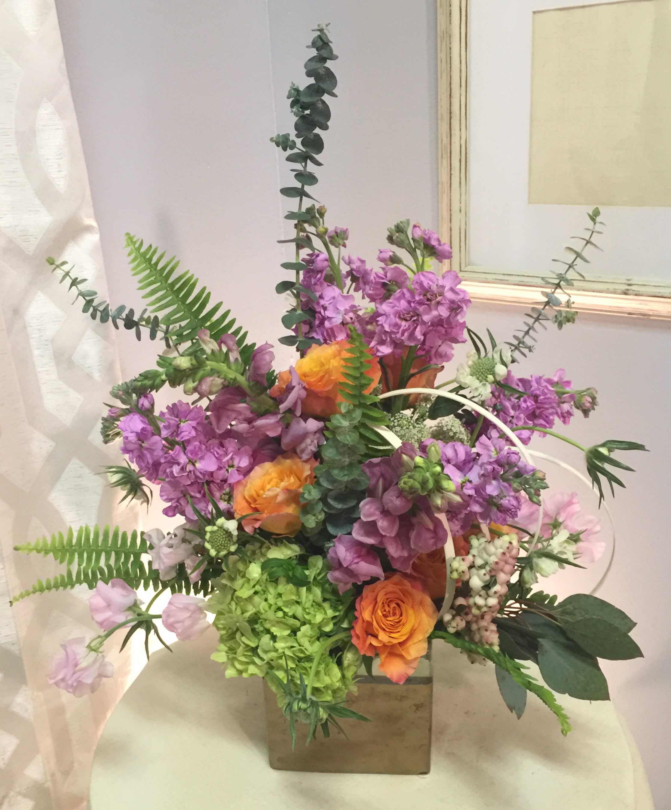 Mixed bouquet with purple flowers and orange roses in a square vase