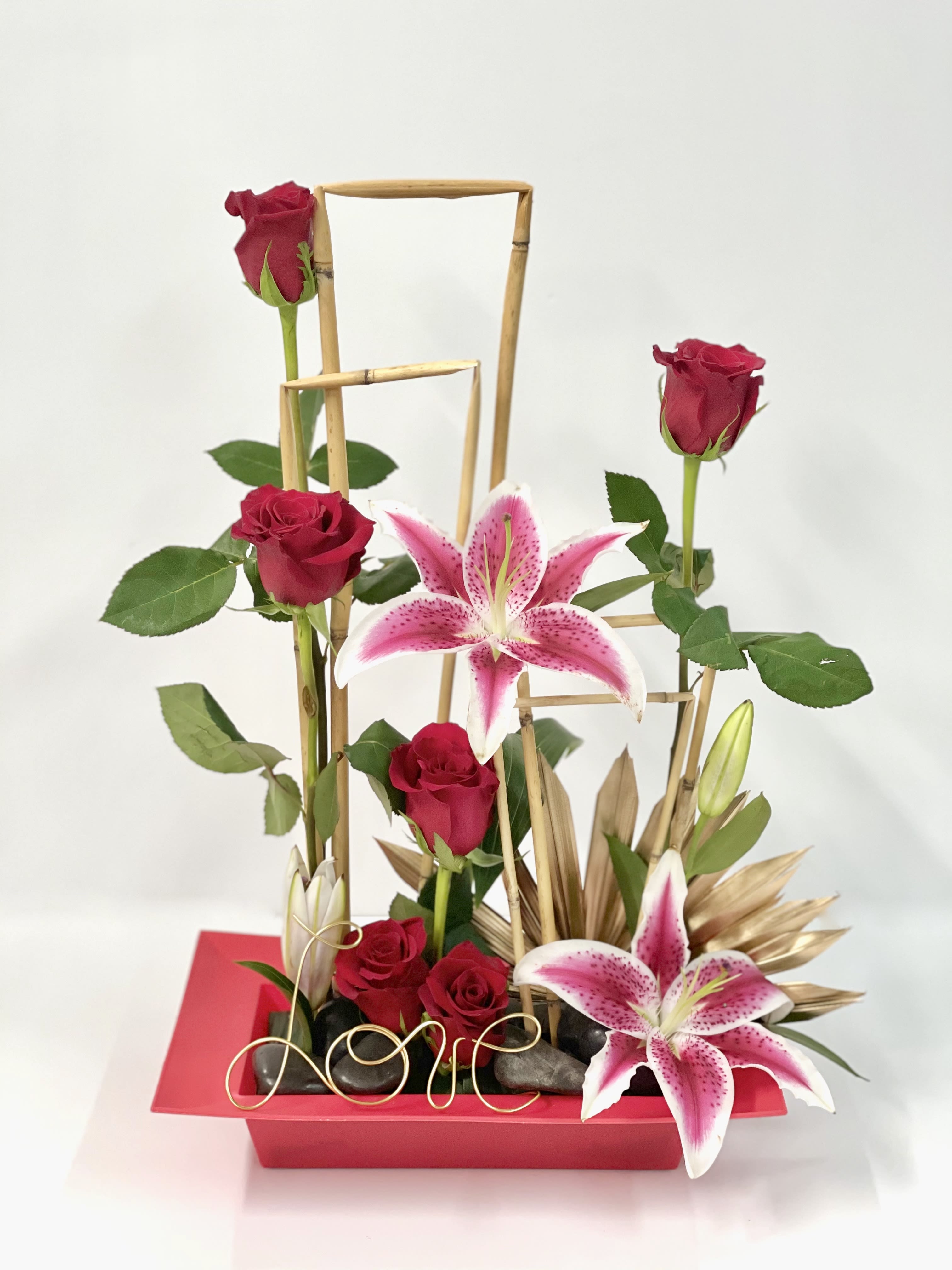 Red roses and pink lilies in a red rectangular vase with bamboo accents