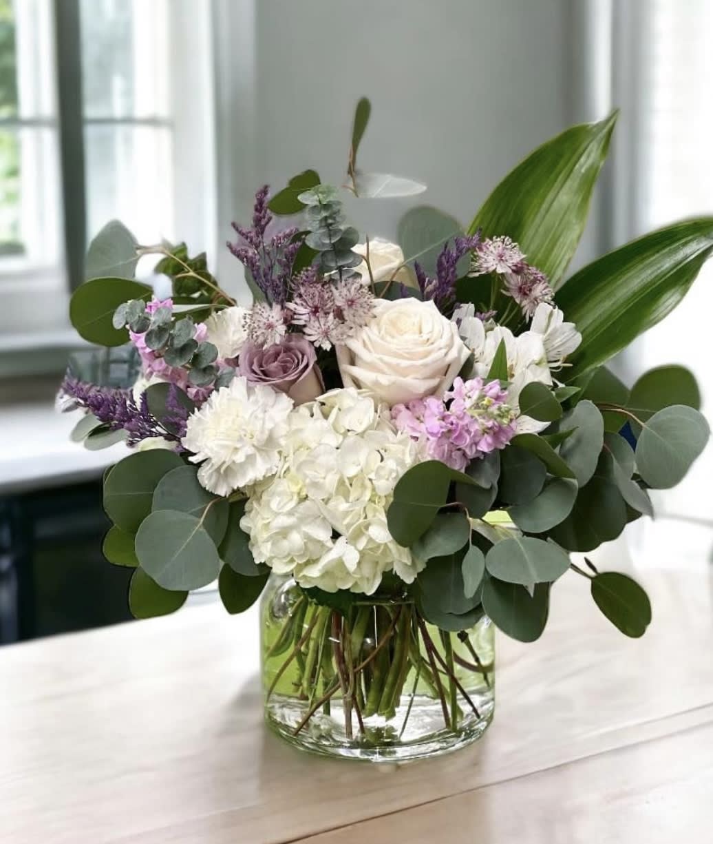 Mixed bouquet of white, blush, and purple flowers in a glass vase