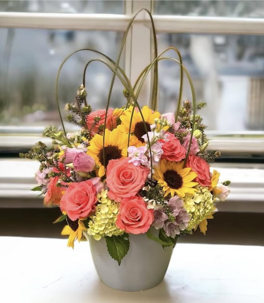 Basket arrangement of pink roses and yellow sunflowers in a gray container