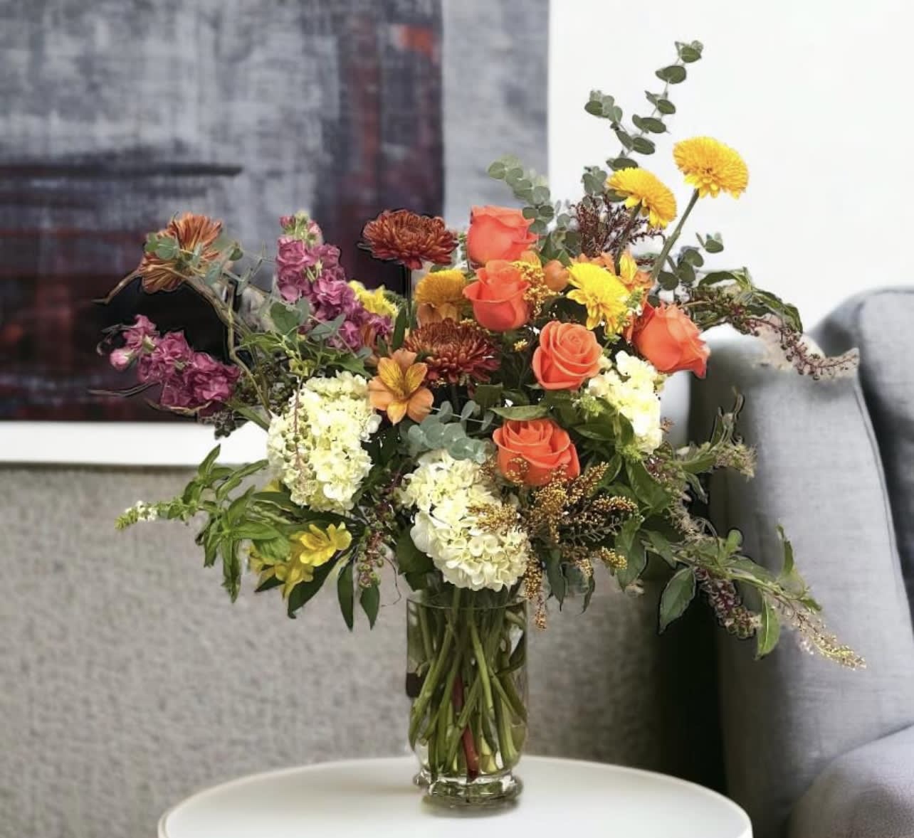 Mixed bouquet of orange roses, yellow mums, and white hydrangeas in a glass vase