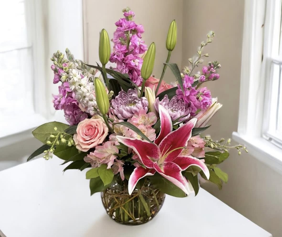 Pink lilies and roses in a glass vase with purple flowers