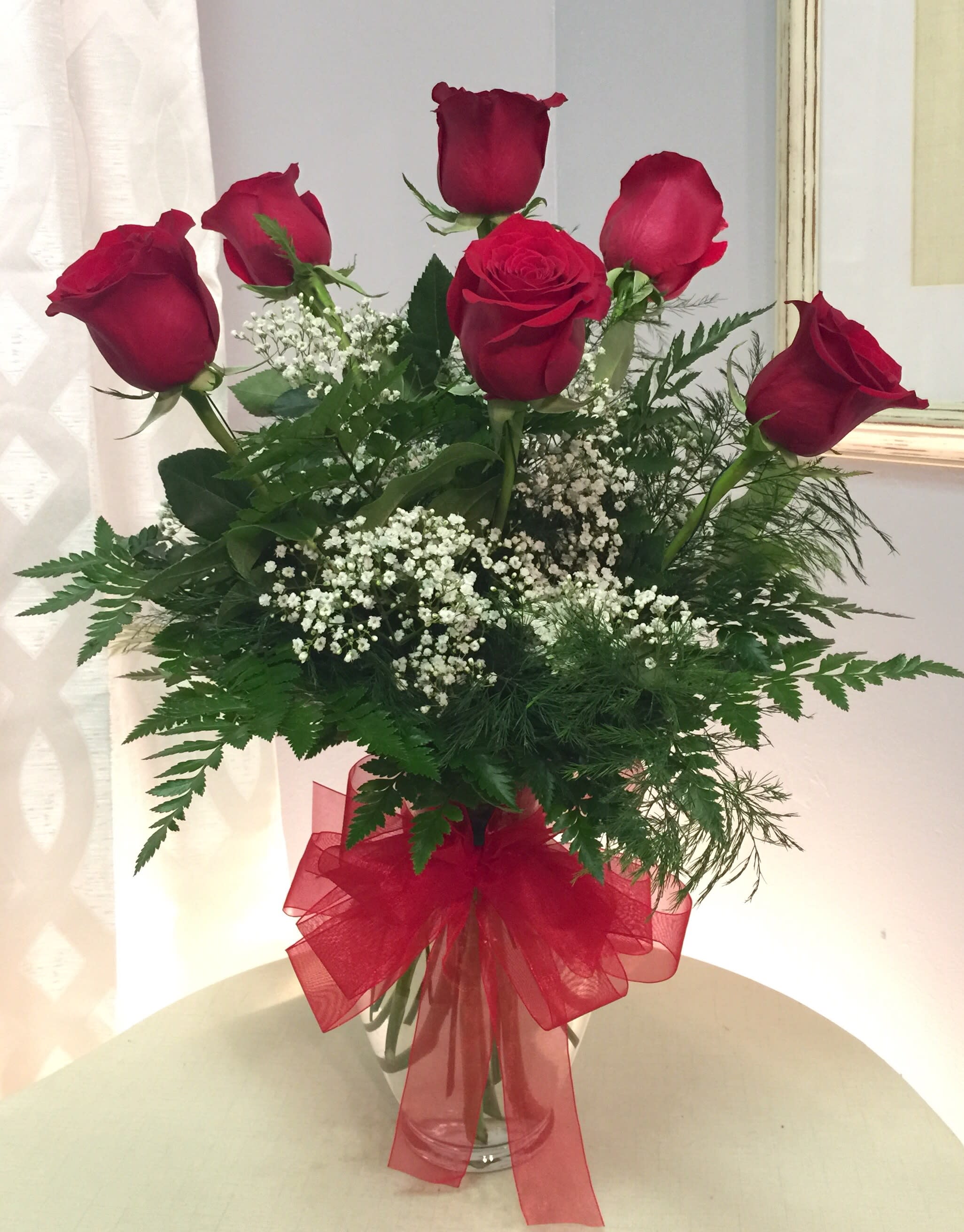 Red roses in a clear vase with baby's breath and a red ribbon