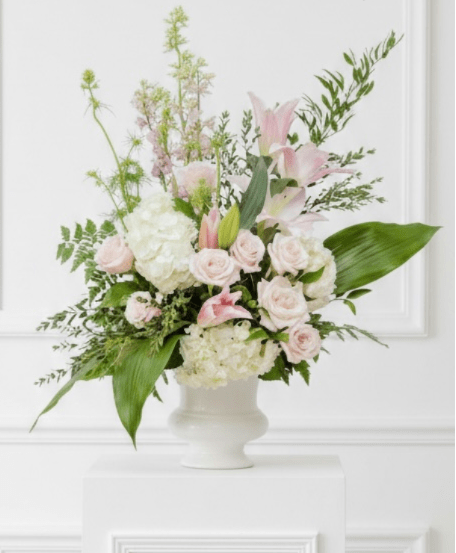 White and Pink Urn - Pale pink lilies and roses with white hydrangeas and greens arranged in a white pedestal vase, airy and elegant
