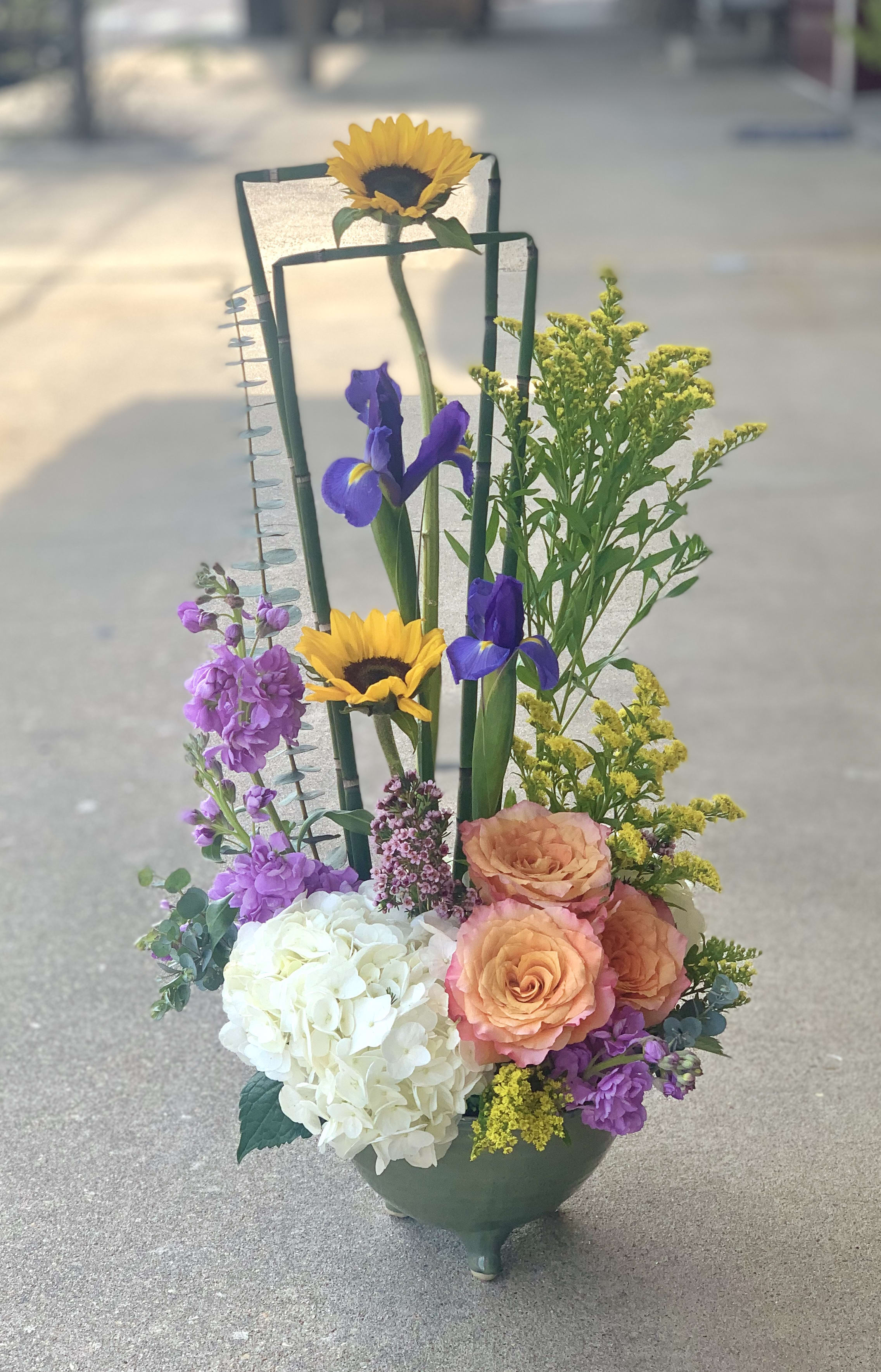 Mixed floral arrangement in a green vase with sunflowers, irises, roses, and hydrangea