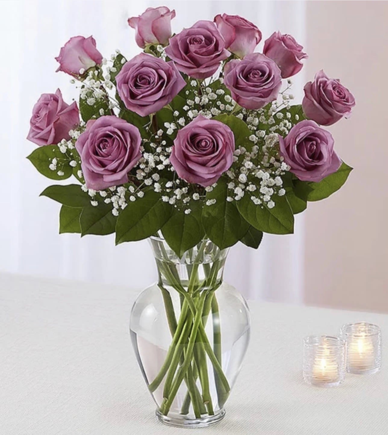 A Dozen Lavender Roses - 12 lavender roses, with variegated pittosporum and salal, arrive in a classic glass urn vase. Approximately 14" W x 16" H