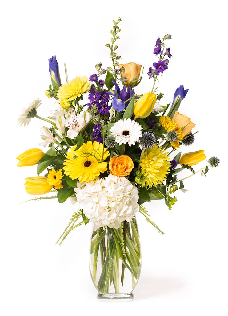 Mixed bouquet of yellow, purple, white, and orange flowers in a clear glass vase