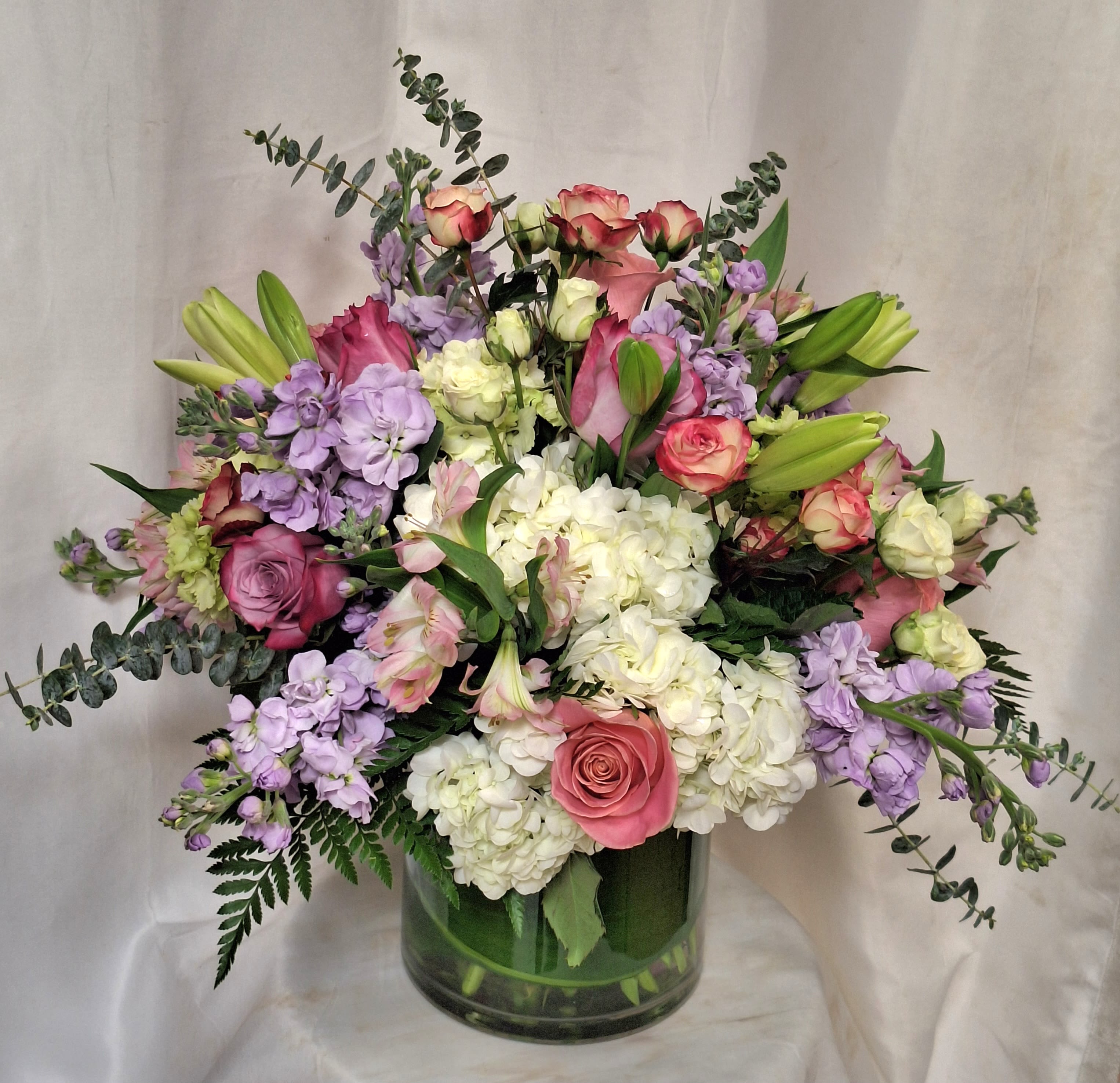 Large mixed arrangement of pink roses, white hydrangeas, lavender blooms and lilies in a clear glass vase