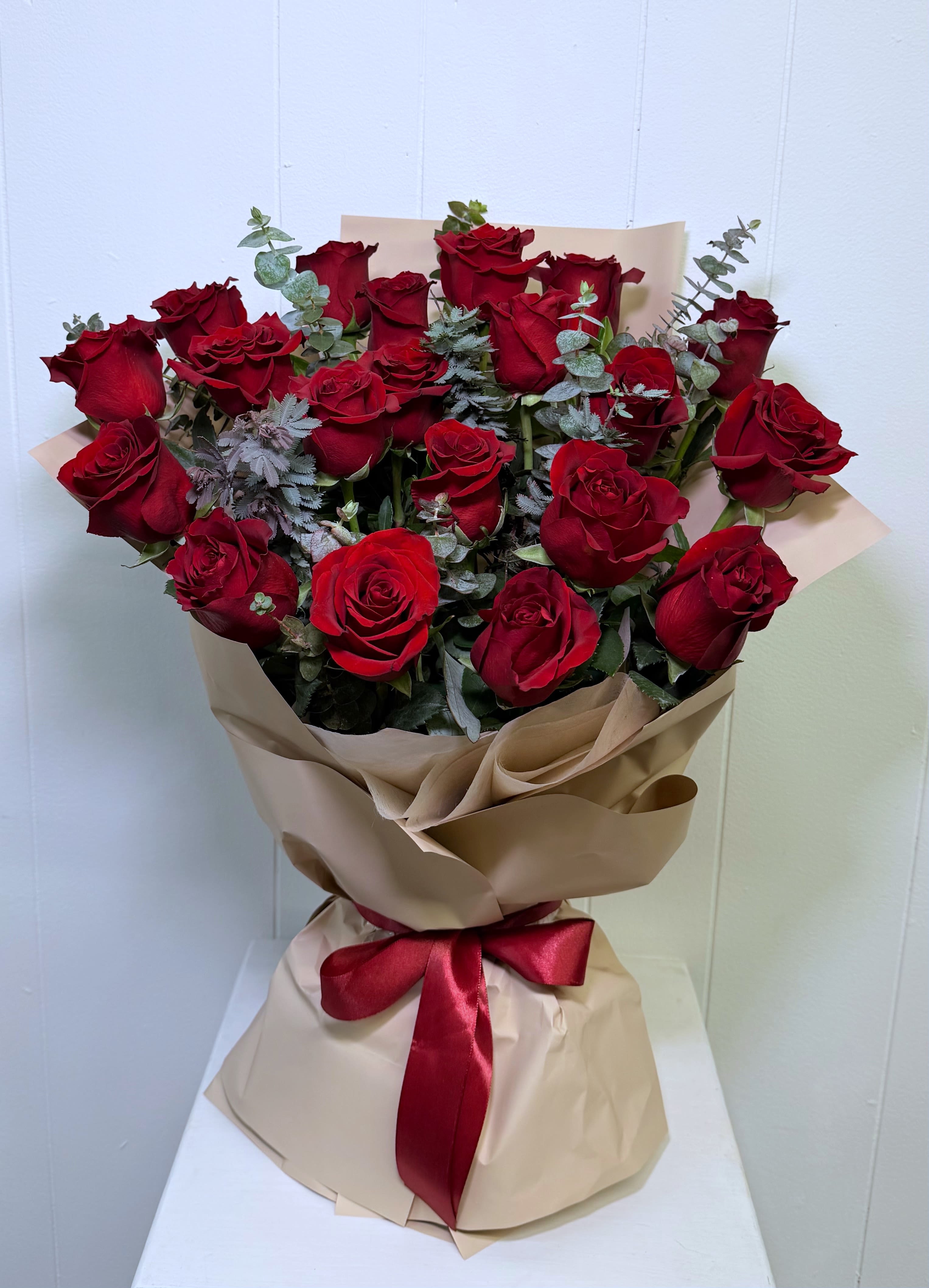 Red Velvet Romance Bouquet - A stunning bouquet featuring 25 premium red roses beautifully arranged with fresh green foliage and wrapped in luxurious high-quality paper. Finished with an elegant satin ribbon bow, this bouquet is designed to make a lasting impression for any romantic occasion.  This is a hand-wrapped bouquet with a hydration base, allowing the flowers to stay fresh without needing to be placed in a vase immediately. Perfect for gifting, easy to transport, and ready to enjoy the moment it arrives.  Elegant, romantic, and timeless — the perfect way to say I love you.
