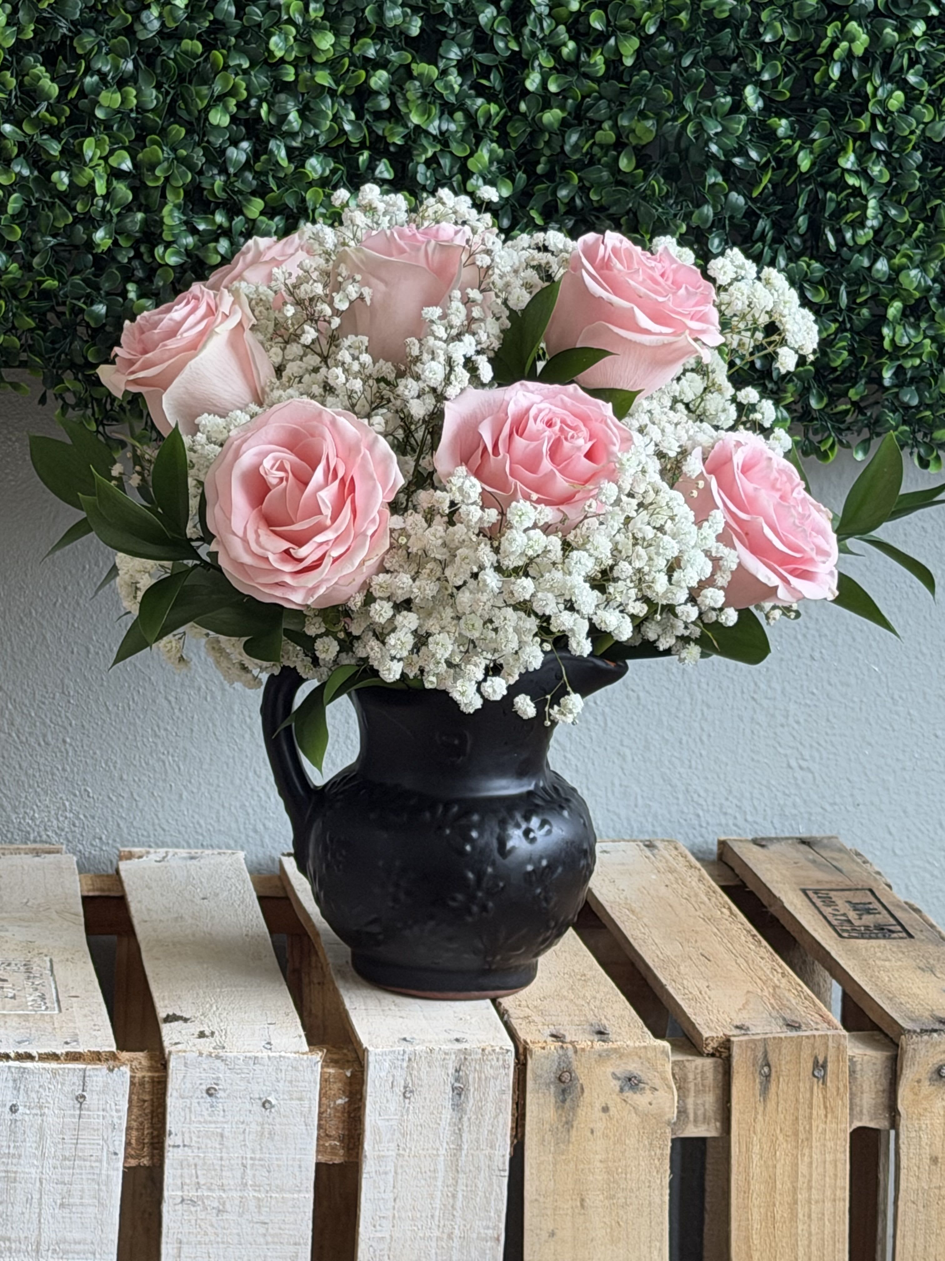 Dark Muse Femme - Soft pink roses gathered into a tight, rounded bouquet create a soft, romantic focal point in this Mother's Day flower arrangement-the kind of gift that will make the person you're thinking of feel genuinely seen. Dark Muse Femme pairs those blushing rose heads with airy white baby's breath and deep green foliage, set in a matte black ceramic vase for a striking pale-on-dark contrast that reads both classic and modern. Perfect for Mother's Day, anniversaries, birthdays, or a thoughtful "just because" moment, it sends a message of tenderness and calm.  The design is full and balanced: clustered rose blooms form the centerpiece while the tiny white filler flowers add a cloudlike texture and delicate movement around each stem. The compact black vase grounds the composition and makes the pastel petals pop, giving the arrangement an elegant yet slightly rustic polish that suits a bedside table, office desk, or entry console. Arranged for immediate display-place in a cool spot away from direct sun, refresh the water every couple of days, and trim stems slightly if needed to extend vase life.