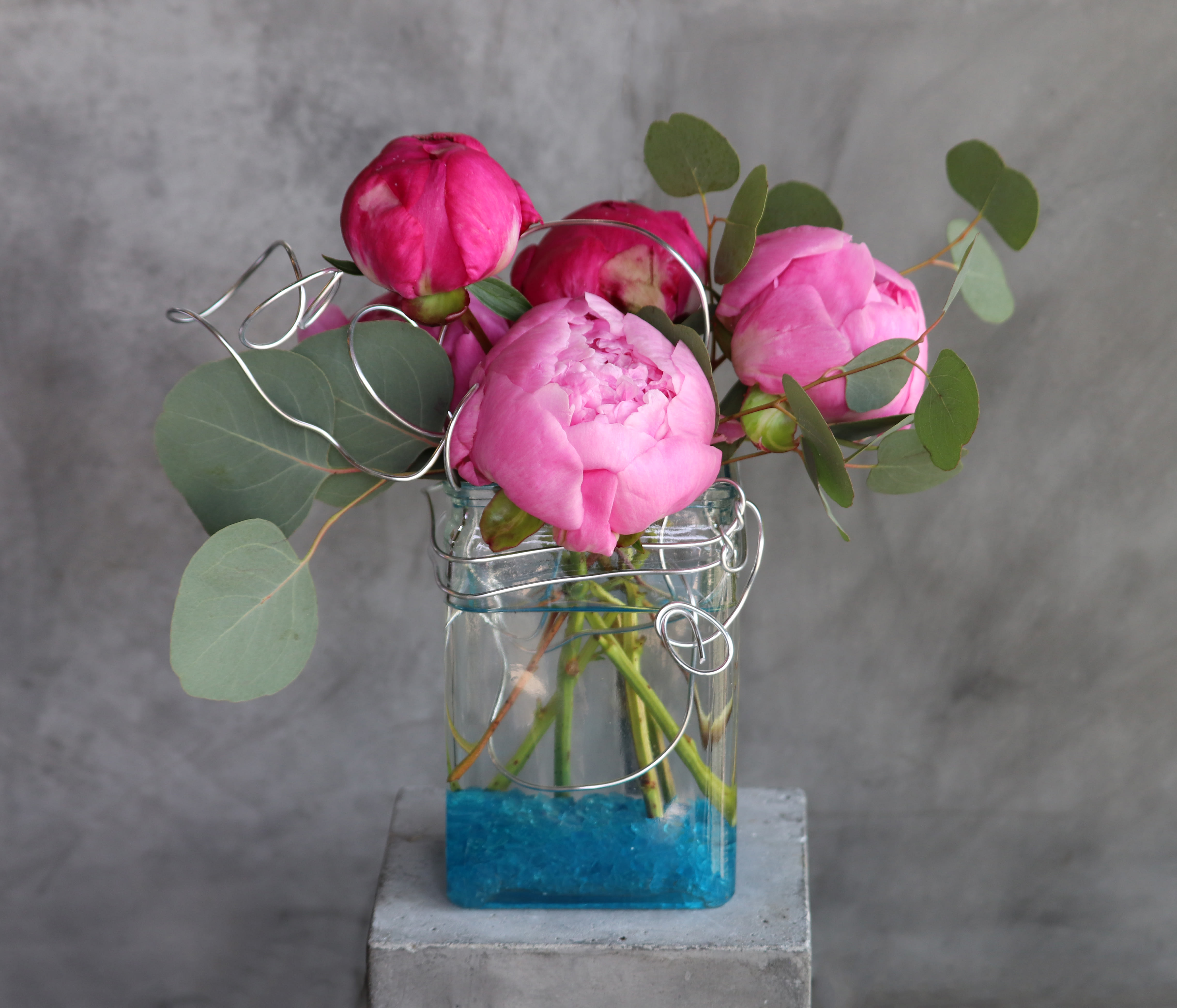 Pink peonies in a clear glass vase with eucalyptus and wire accents