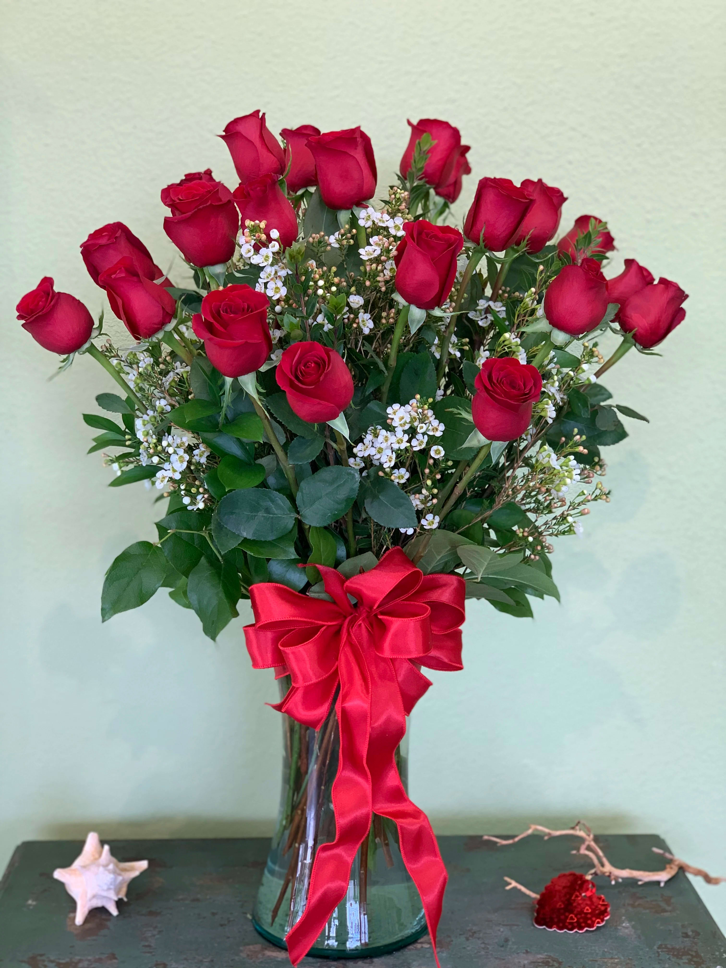 Red roses arranged in a glass vase with a red ribbon bow