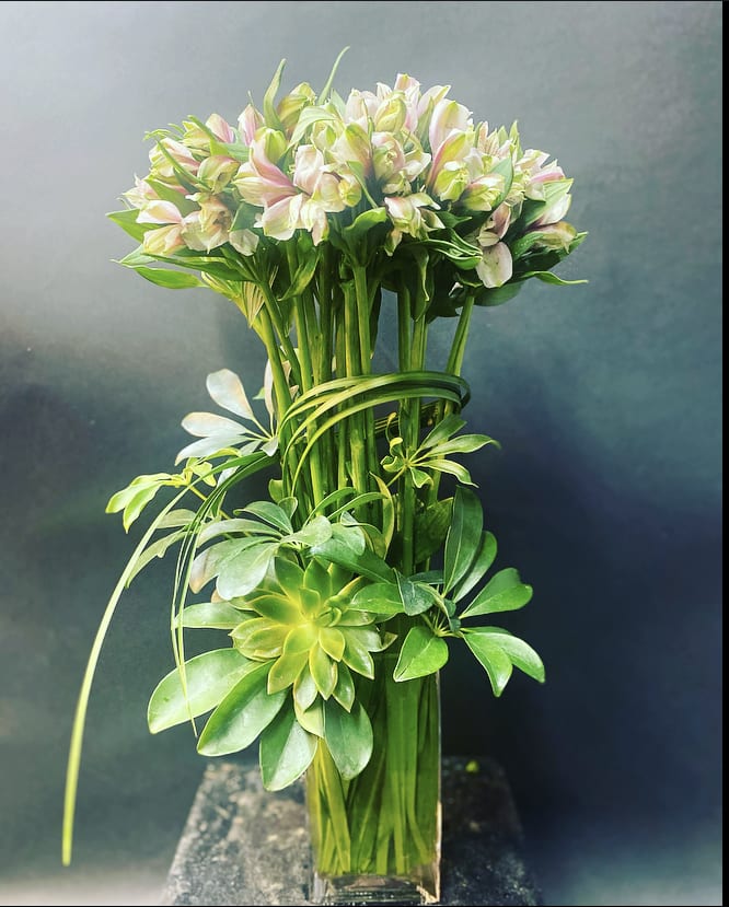 Tall bouquet of pale pink and white flowers with green foliage in a clear vase