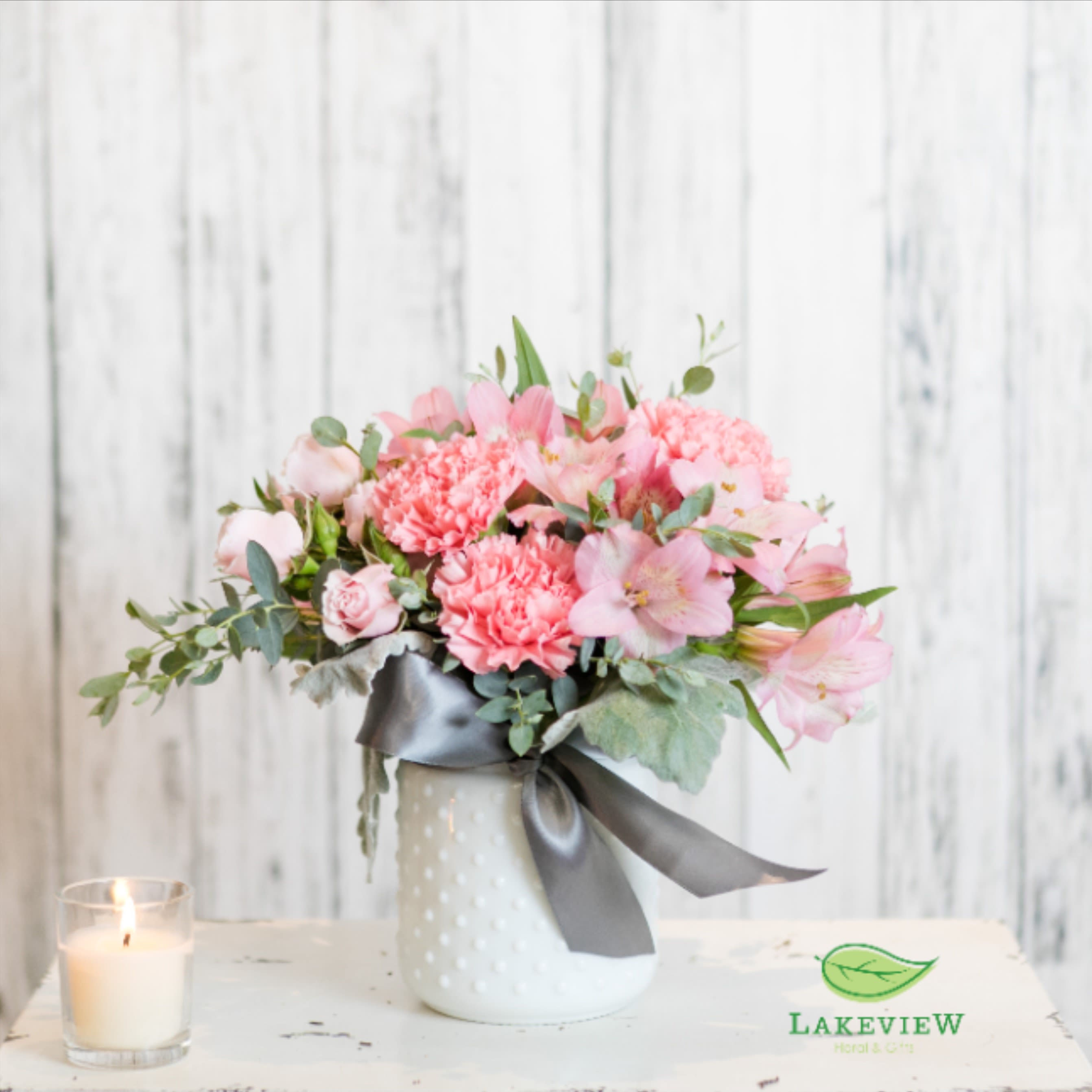 Pink floral arrangement in a white vase with a gray ribbon