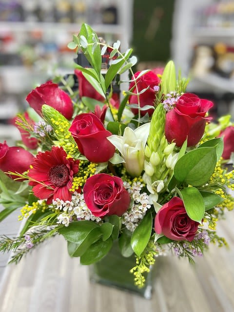 Red rose and white lily arrangement with accent blooms in a clear glass cube vase