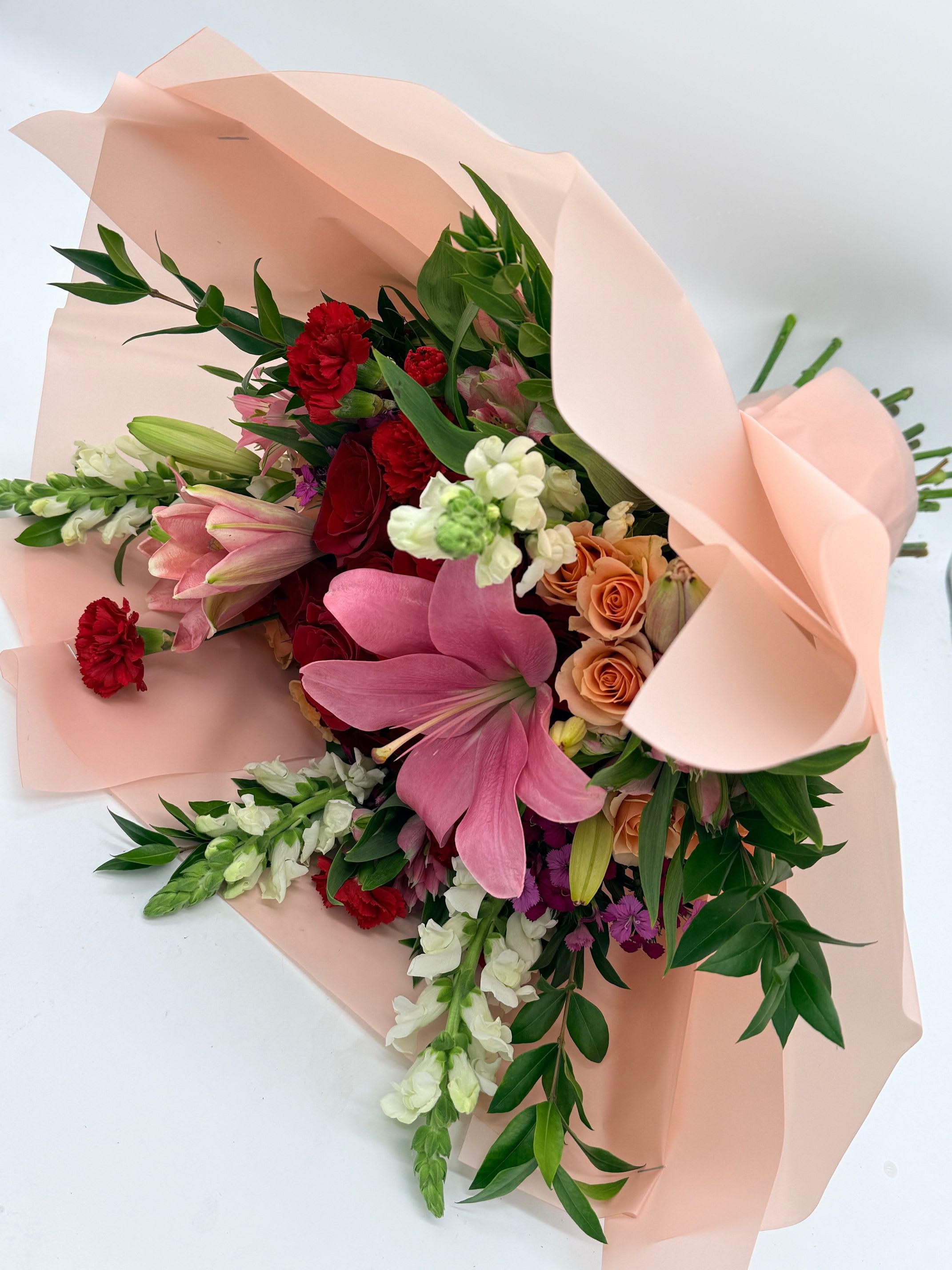 Bouquet of pink lilies, red carnations, and peach roses wrapped in blush paper