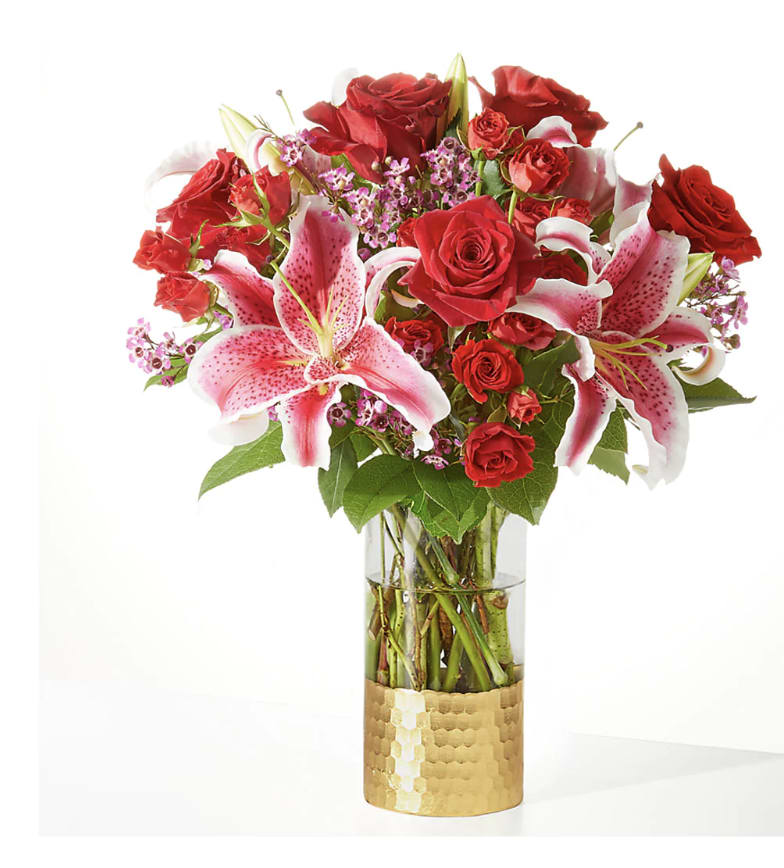 Red roses and pink lilies arranged in a glass vase with a gold base