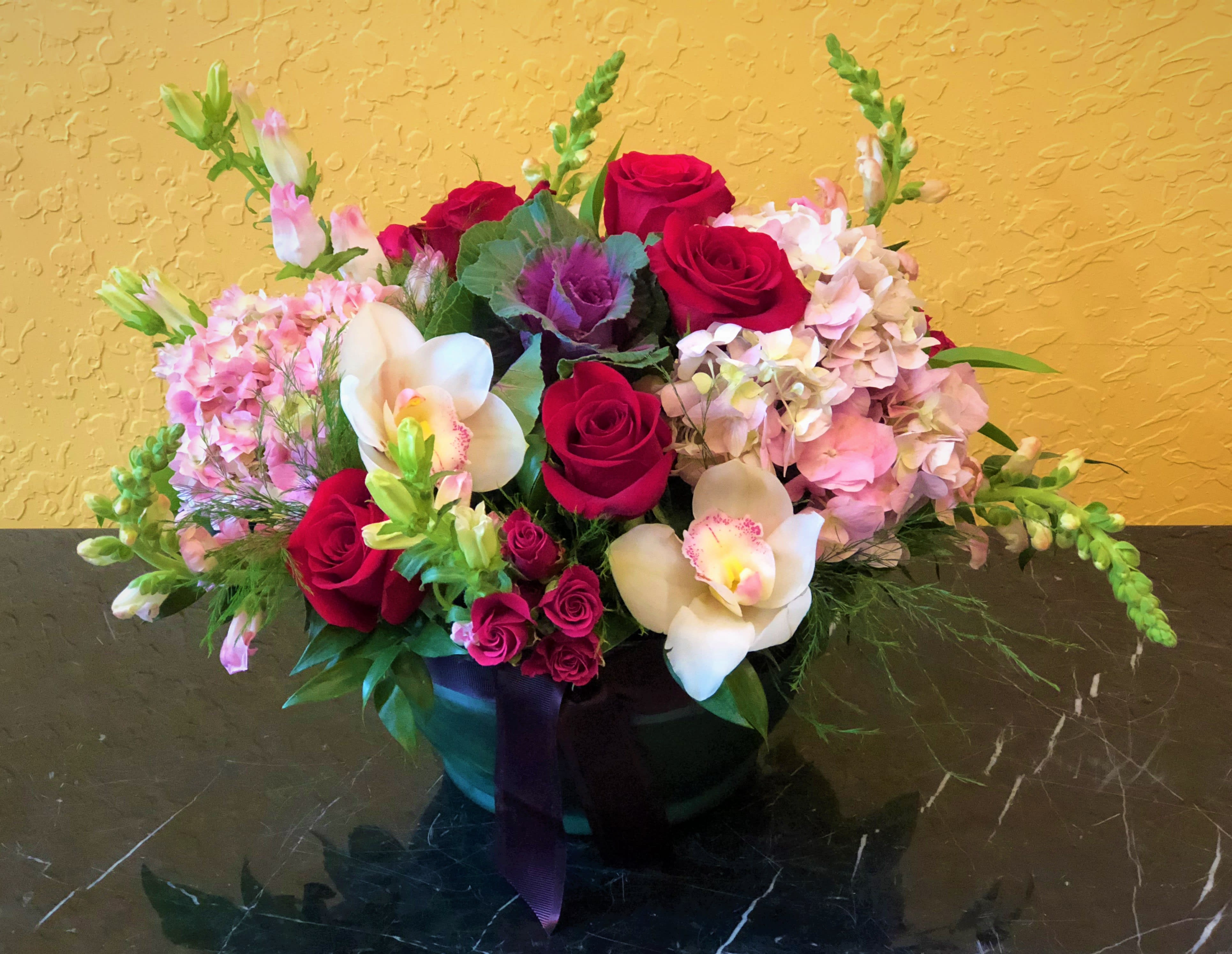 Mixed bouquet of red roses, pink hydrangeas, and white orchids in a black vase