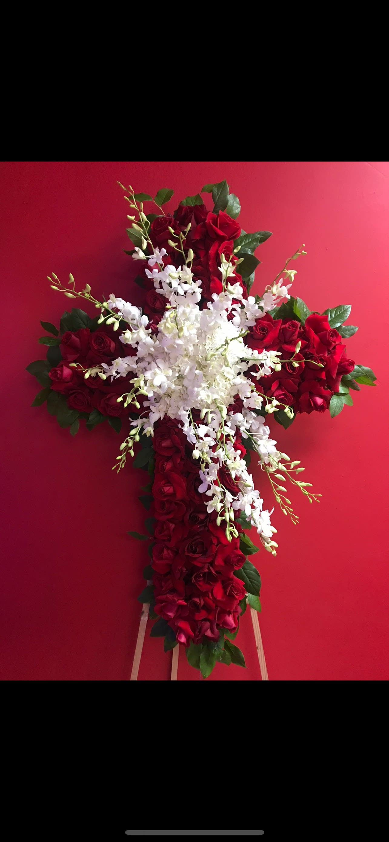Cross-shaped floral arrangement of red roses and white orchids on an easel