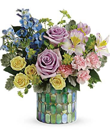 Mixed bouquet of roses, lilies, and blue flowers in a mosaic vase