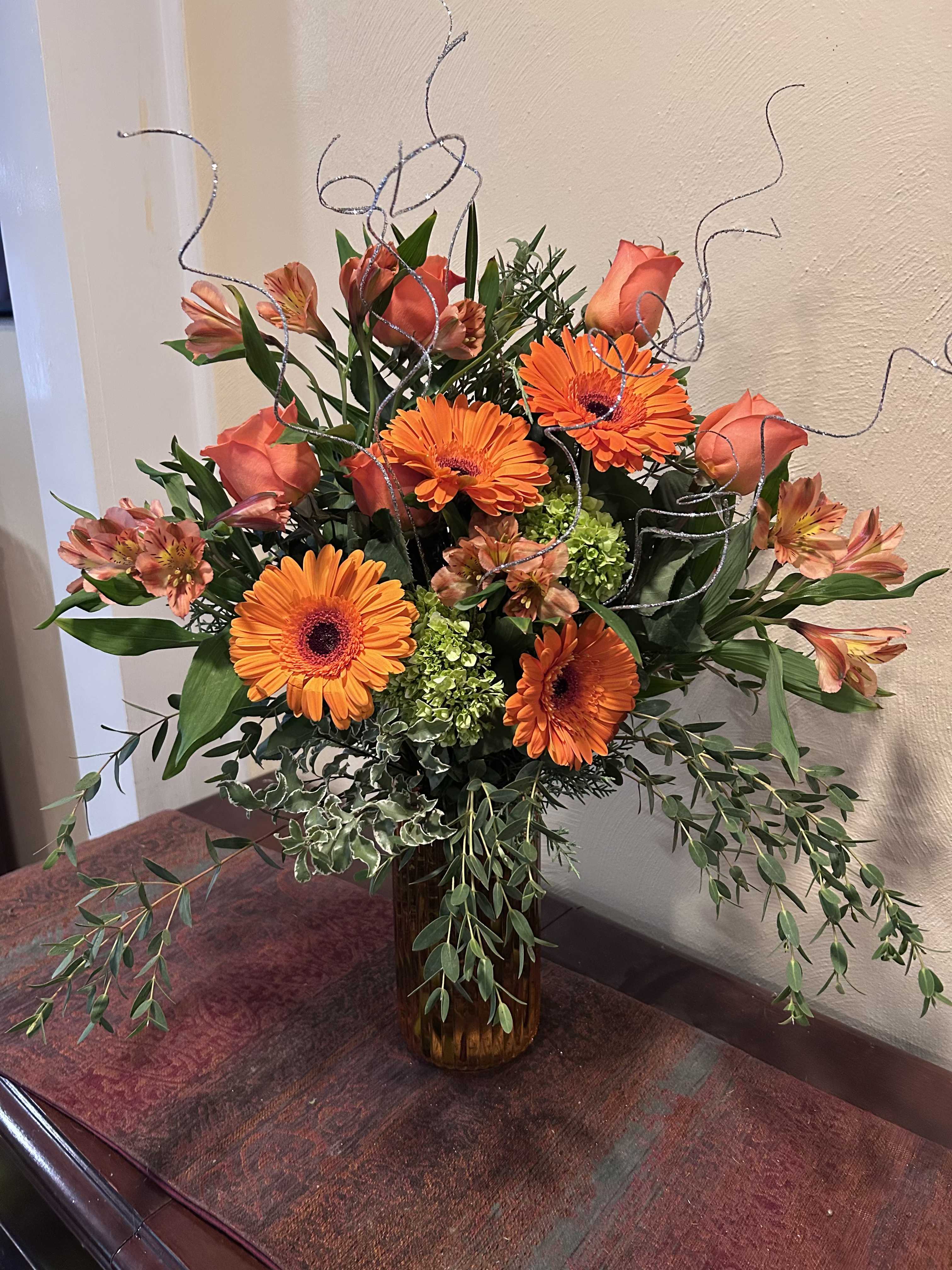 Orange gerbera daisies and roses in a glass vase