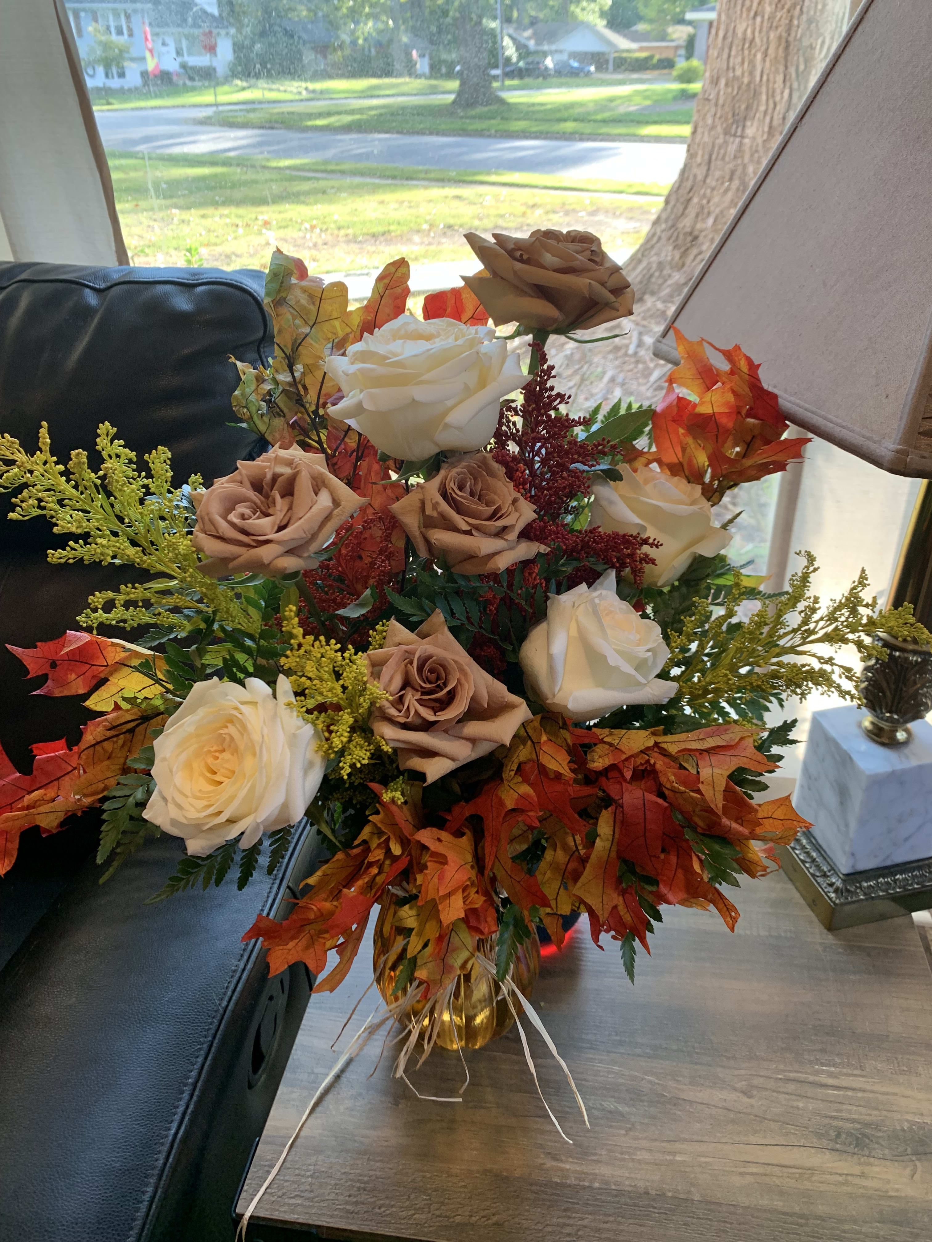 Bouquet of cream and tan roses with autumn leaves in a glass vase