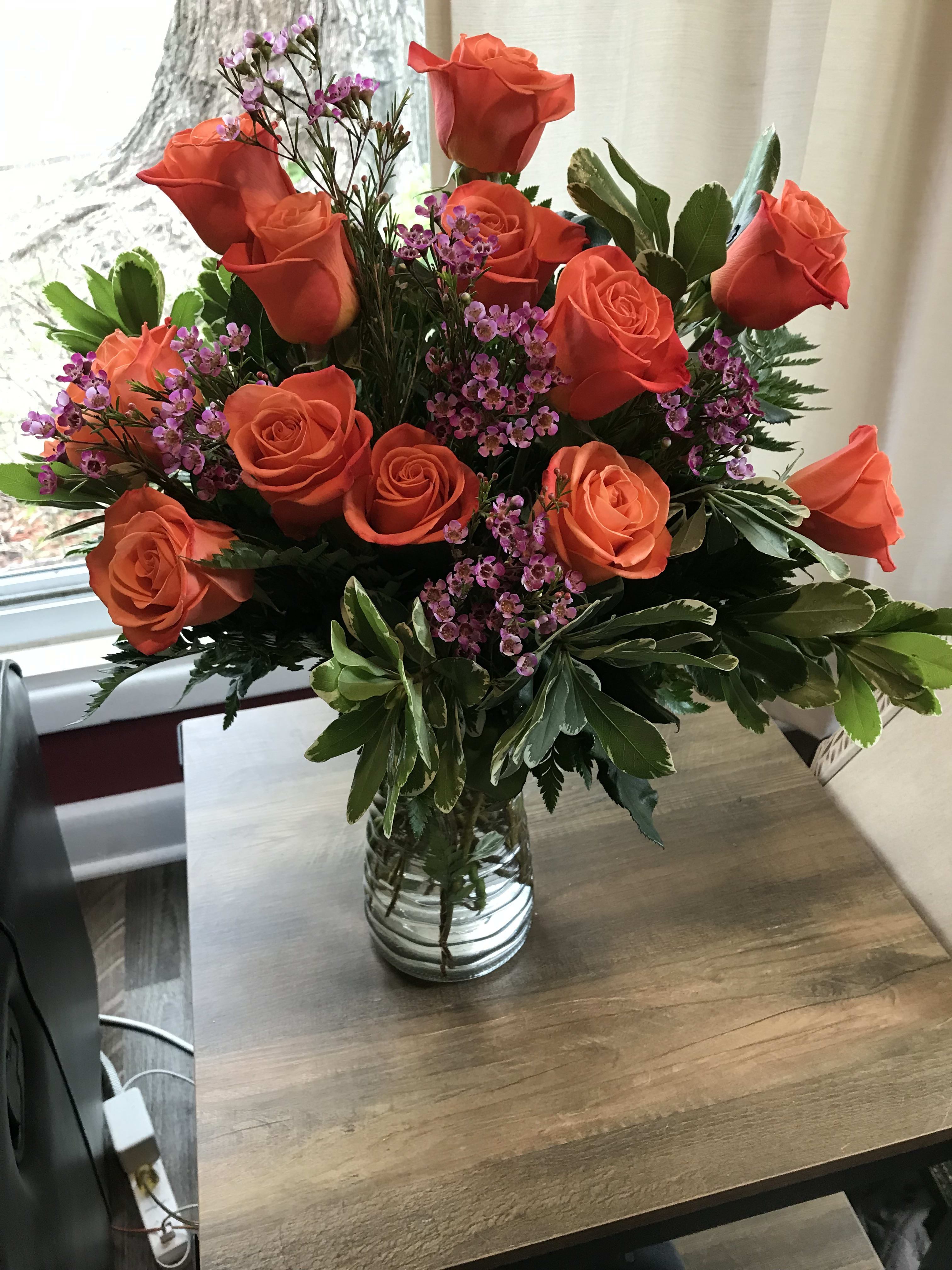 Orange roses and purple filler flowers in a clear glass vase