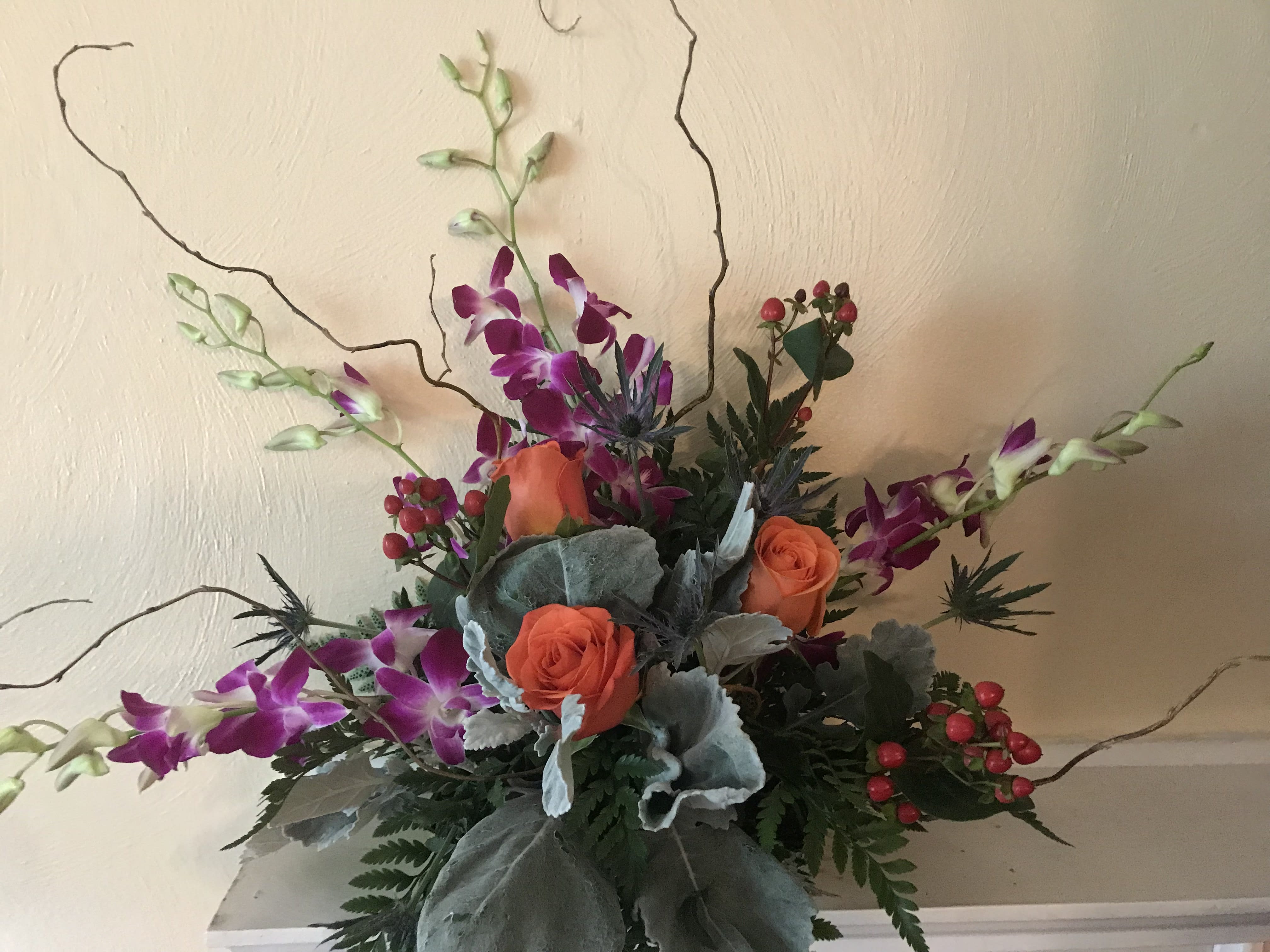 Arrangement of orange roses and purple orchids in a low container