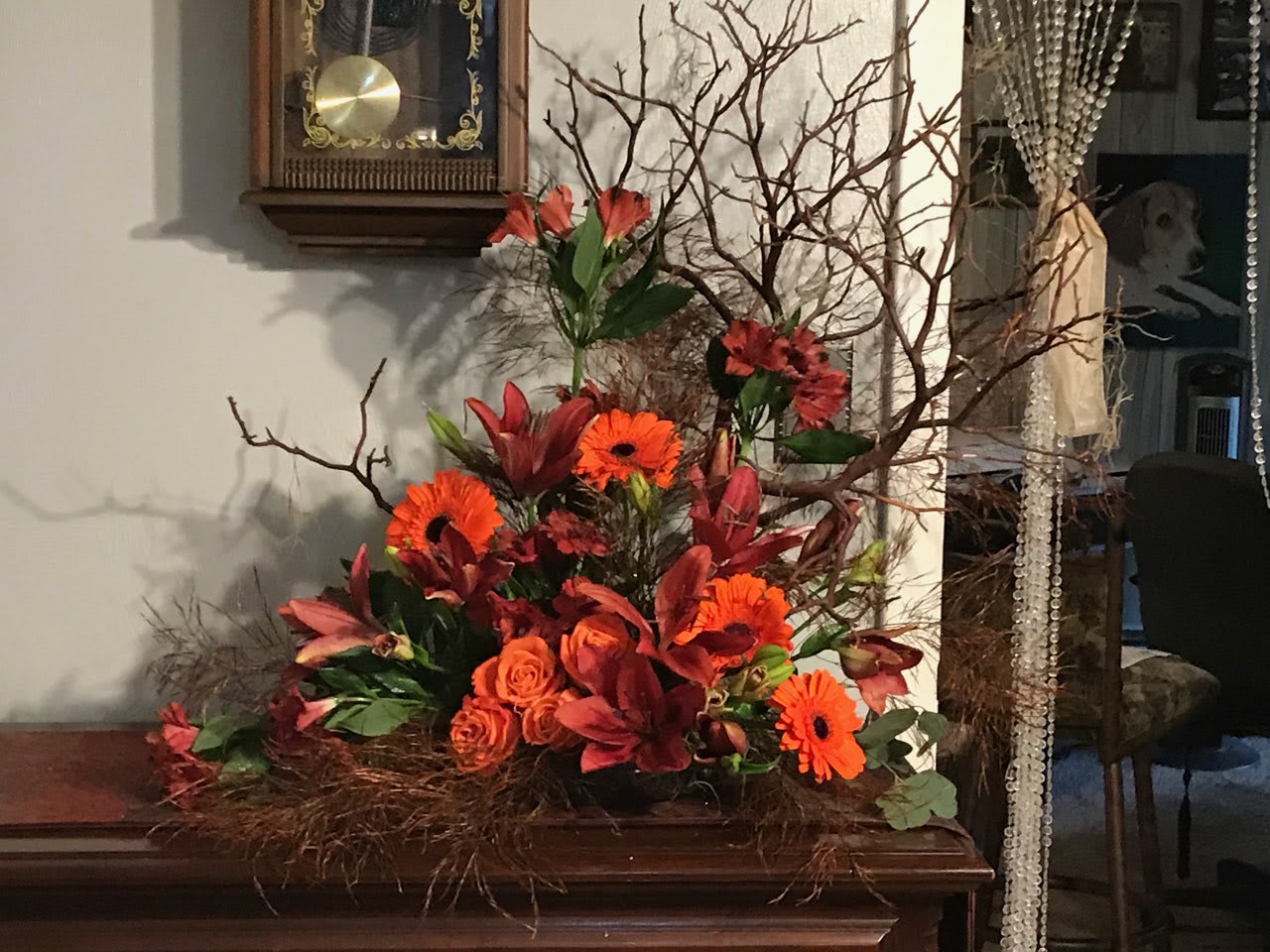 Orange and red floral arrangement with branches in a low container