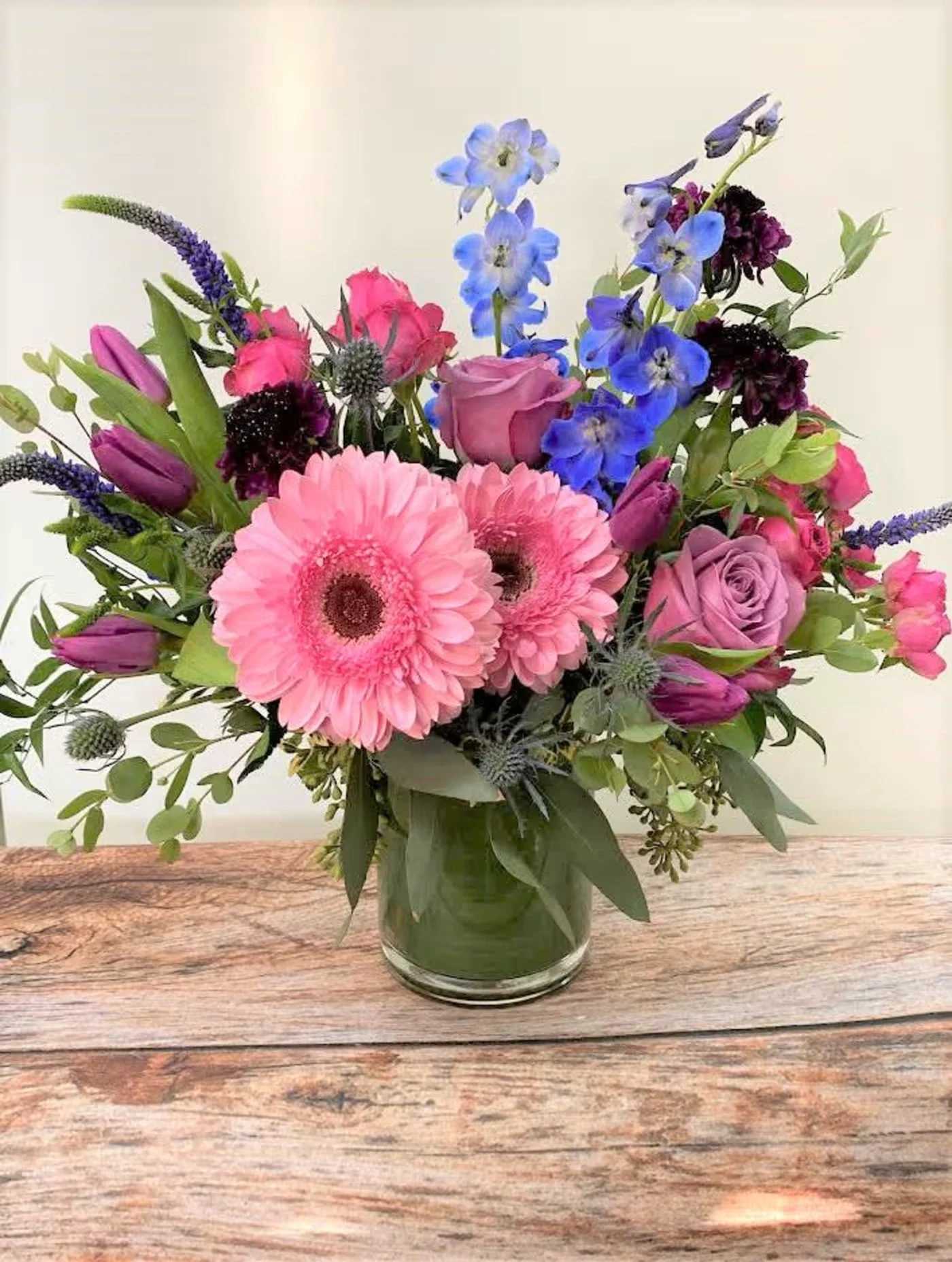 Mixed pink, purple, and blue flowers arranged in a clear glass vase