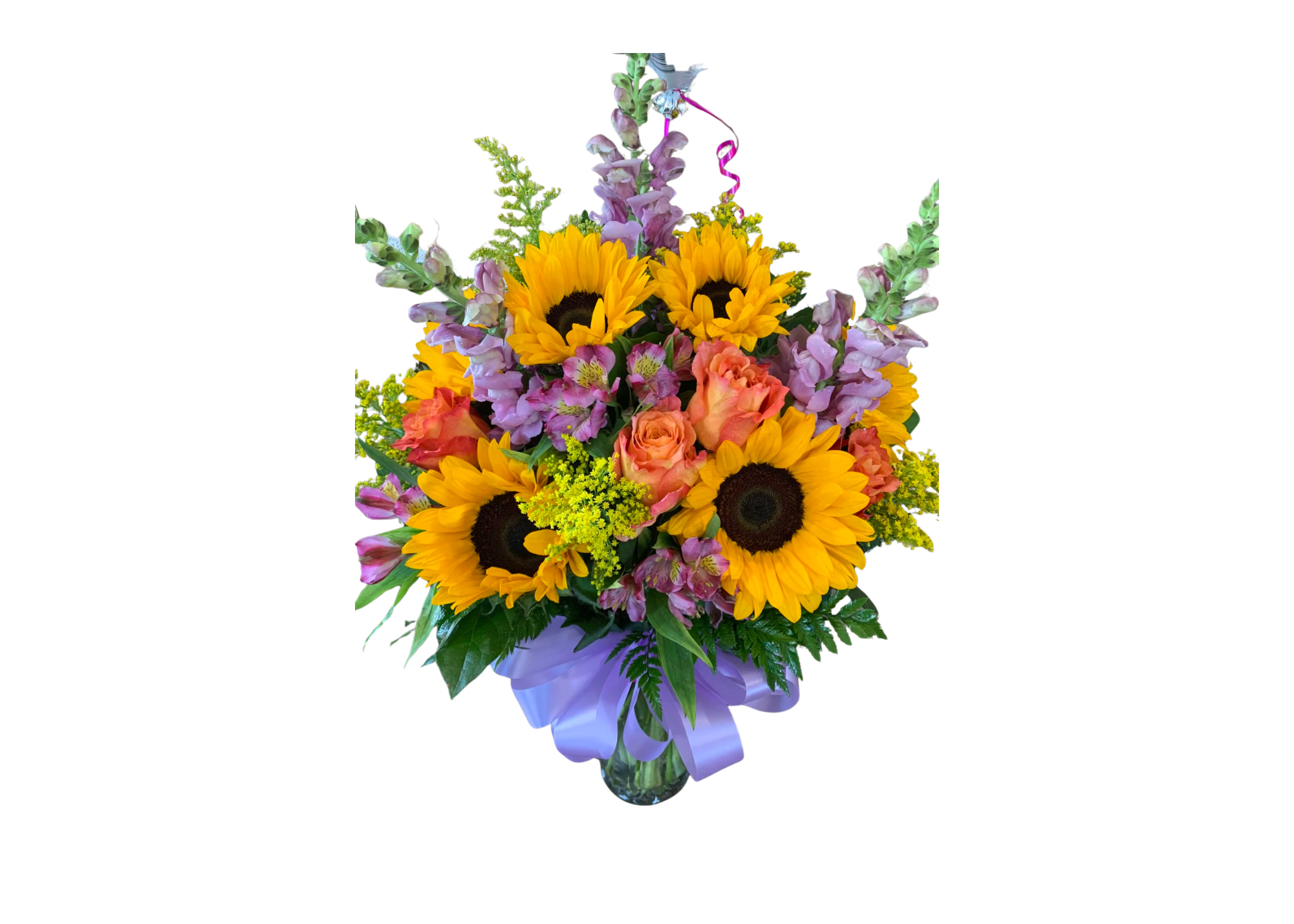 Mixed bouquet of sunflowers, orange roses, and purple flowers in a glass vase with a lavender bow