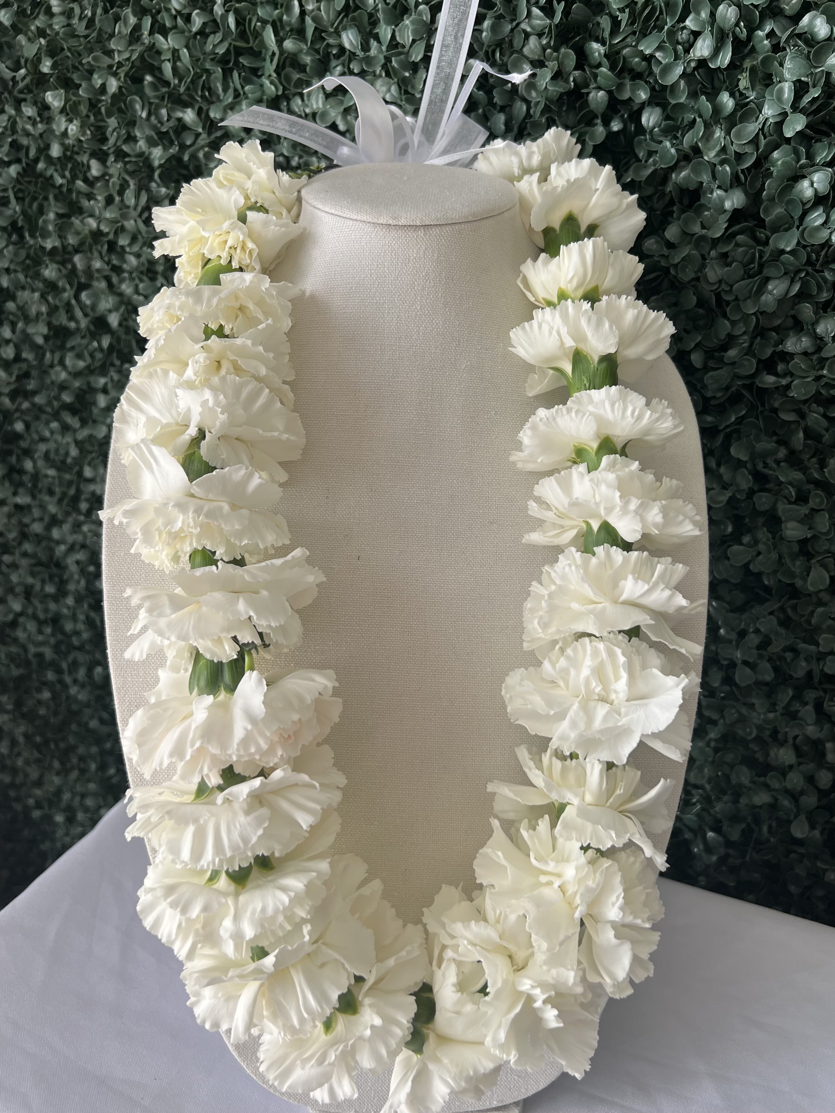 White carnation lei draped over a beige display bust