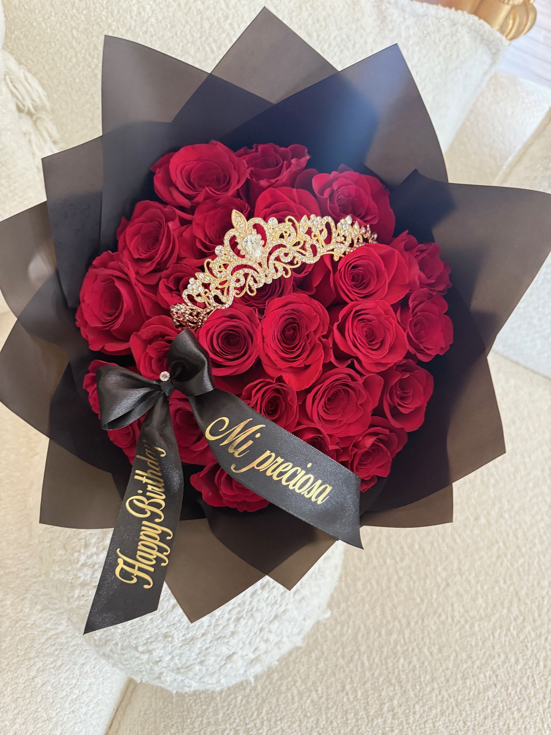 Bouquet of red roses wrapped in black paper with a tiara and ribbon