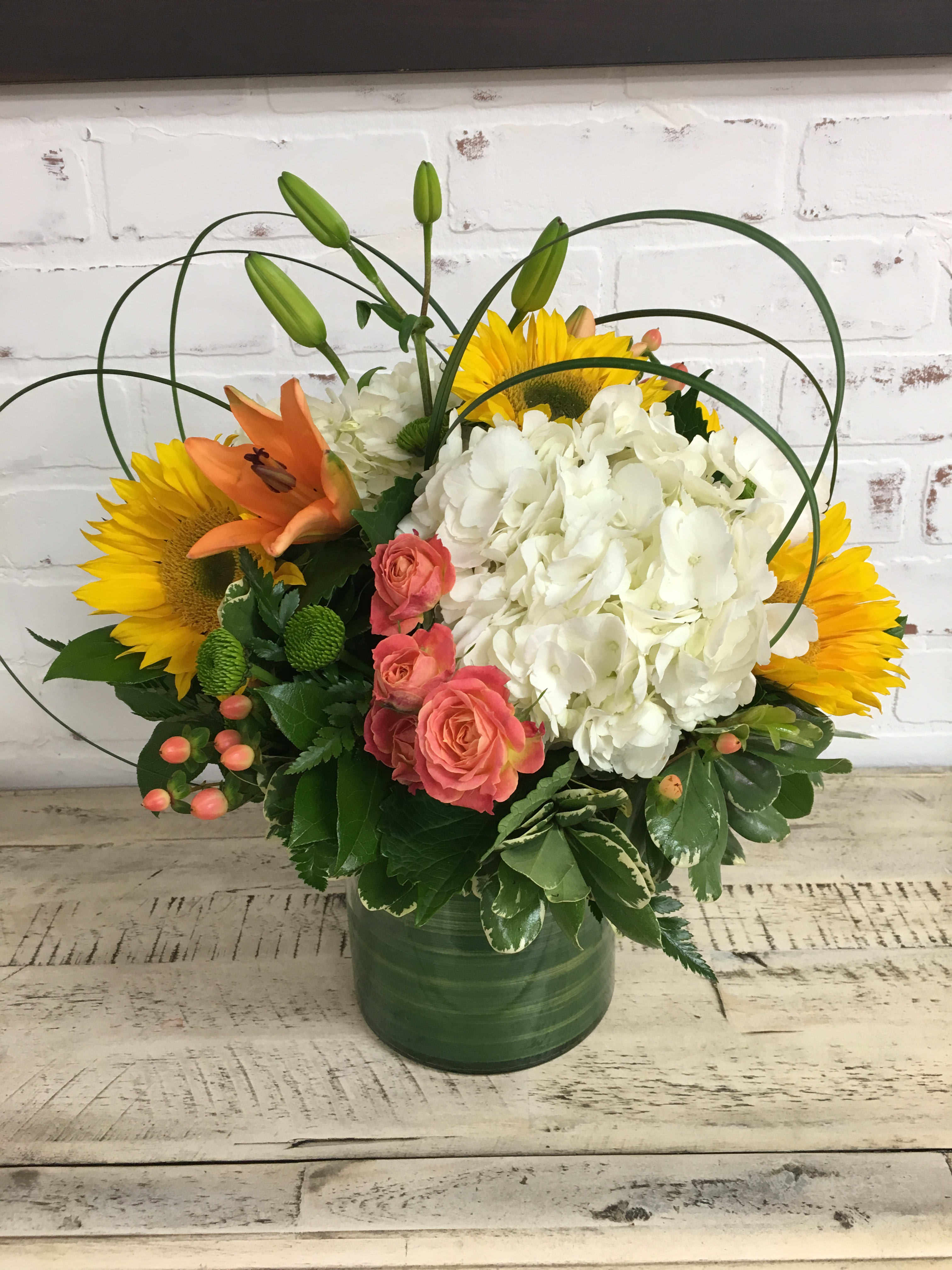 Bouquet of sunflowers, white hydrangea, pink roses, and orange lilies in a green vase