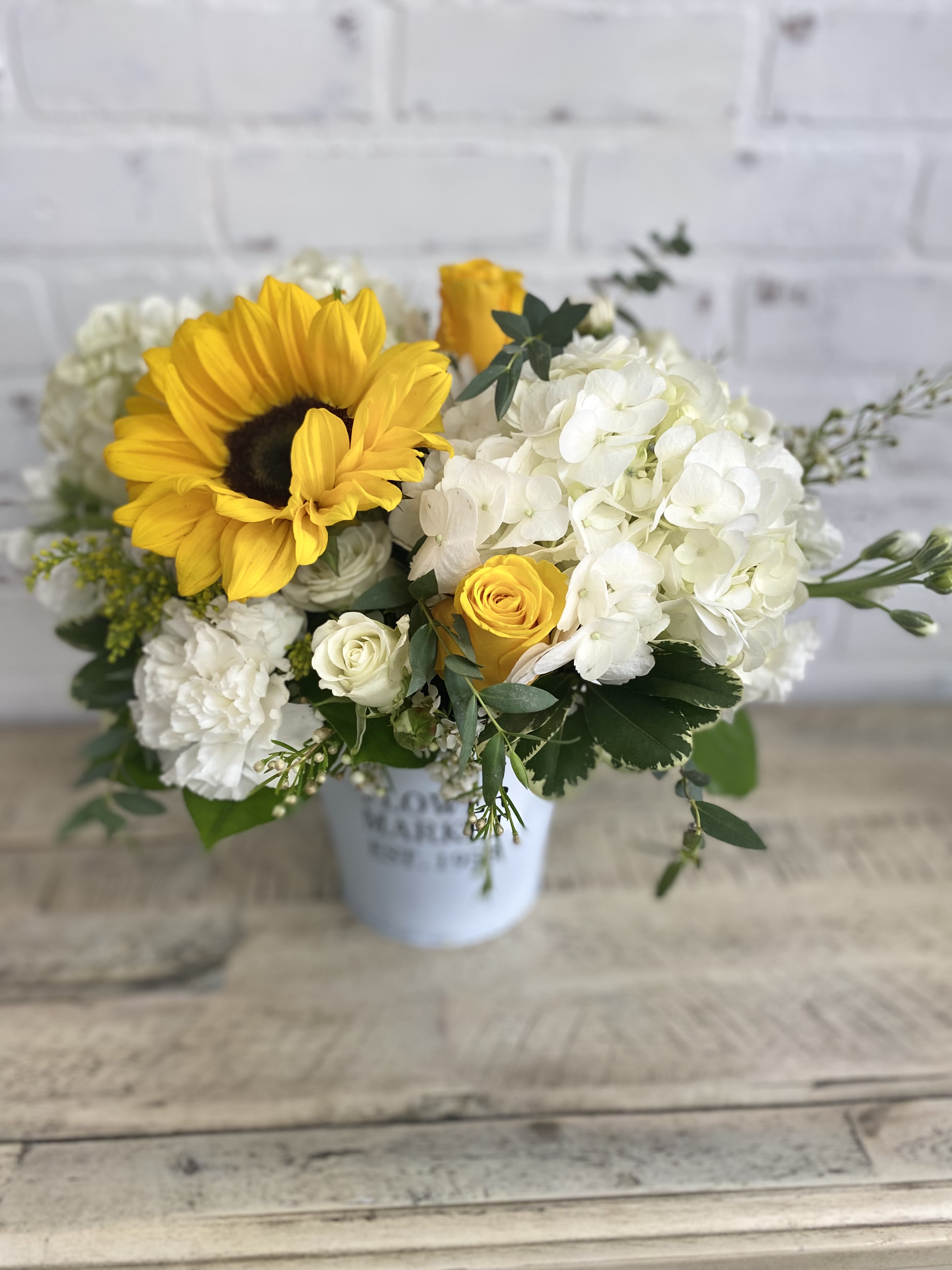 Sunflower and white hydrangea bouquet in a white container