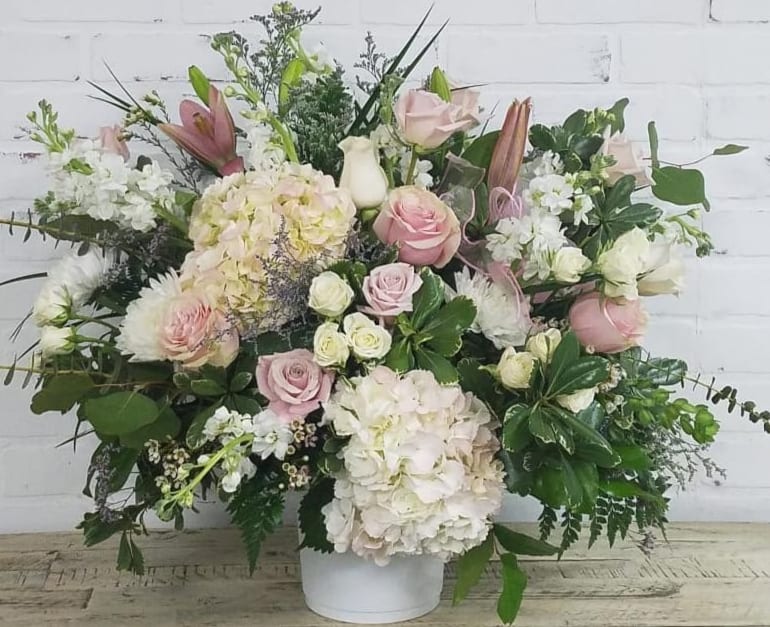 Large pastel bouquet with roses, hydrangeas, and lilies in a white container