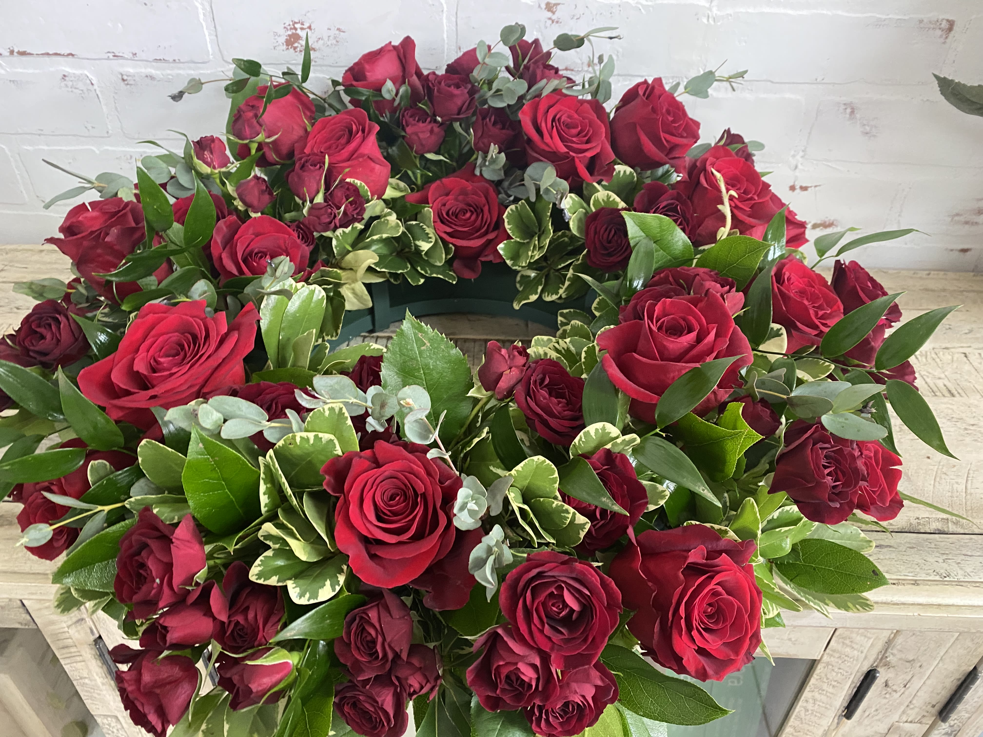 Circular wreath of red roses with mixed greenery on a white surface