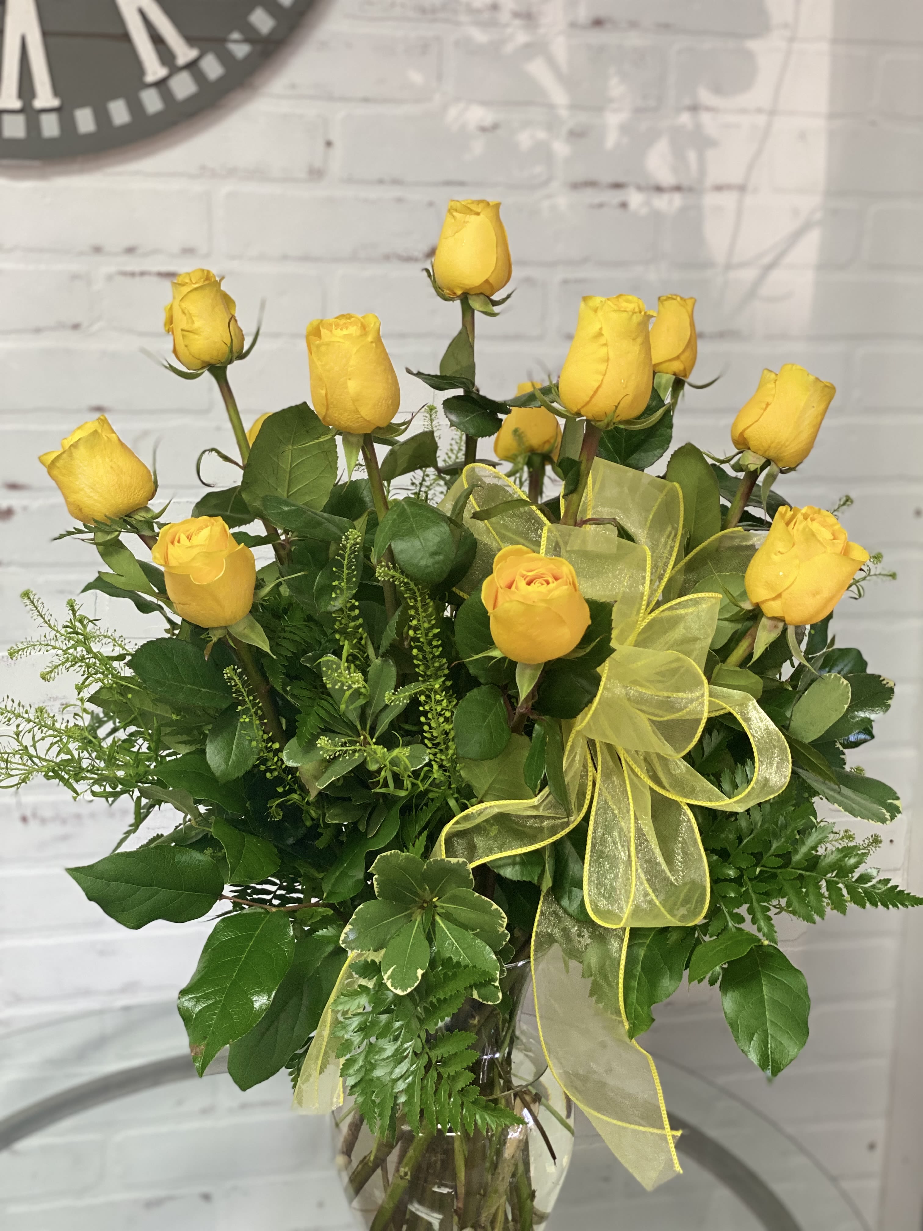 Yellow roses arranged in a clear glass vase with a yellow ribbon