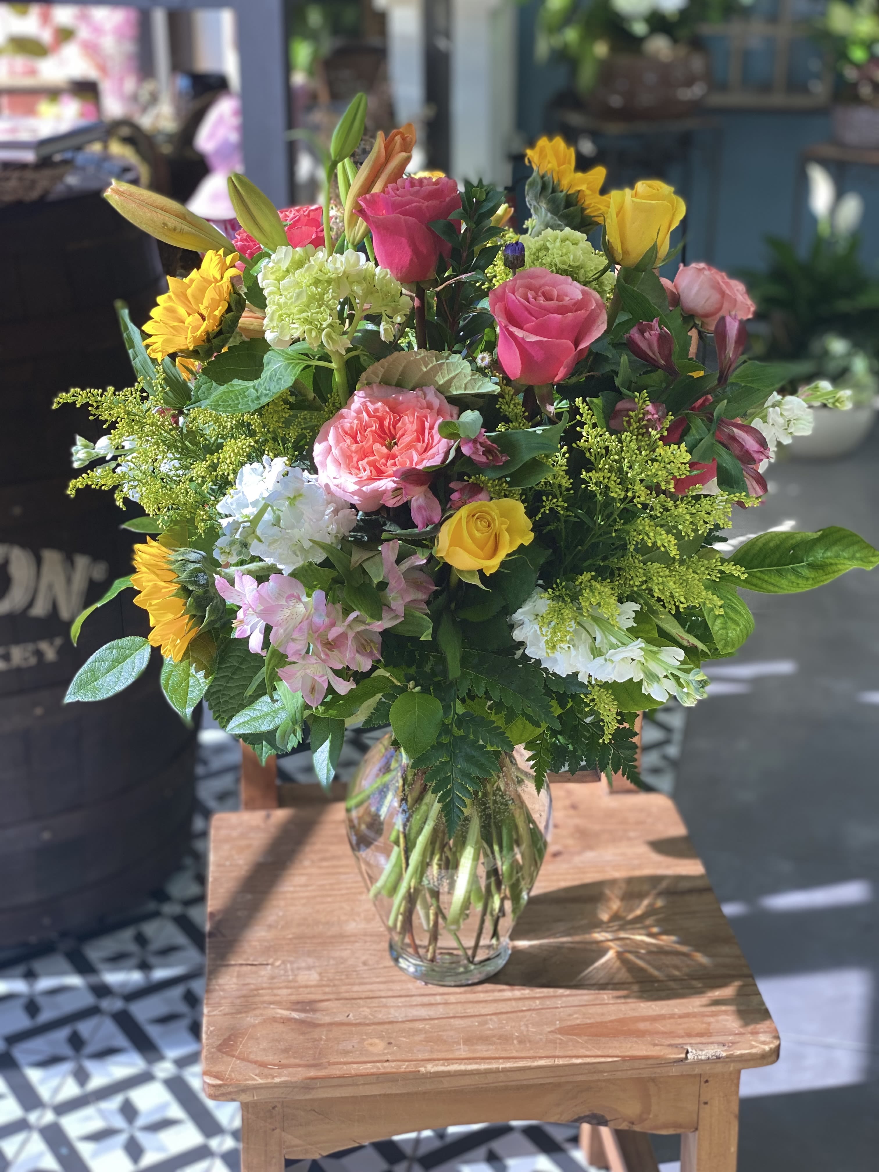 Mixed bouquet of roses, lilies, sunflowers, and hydrangeas in a glass vase