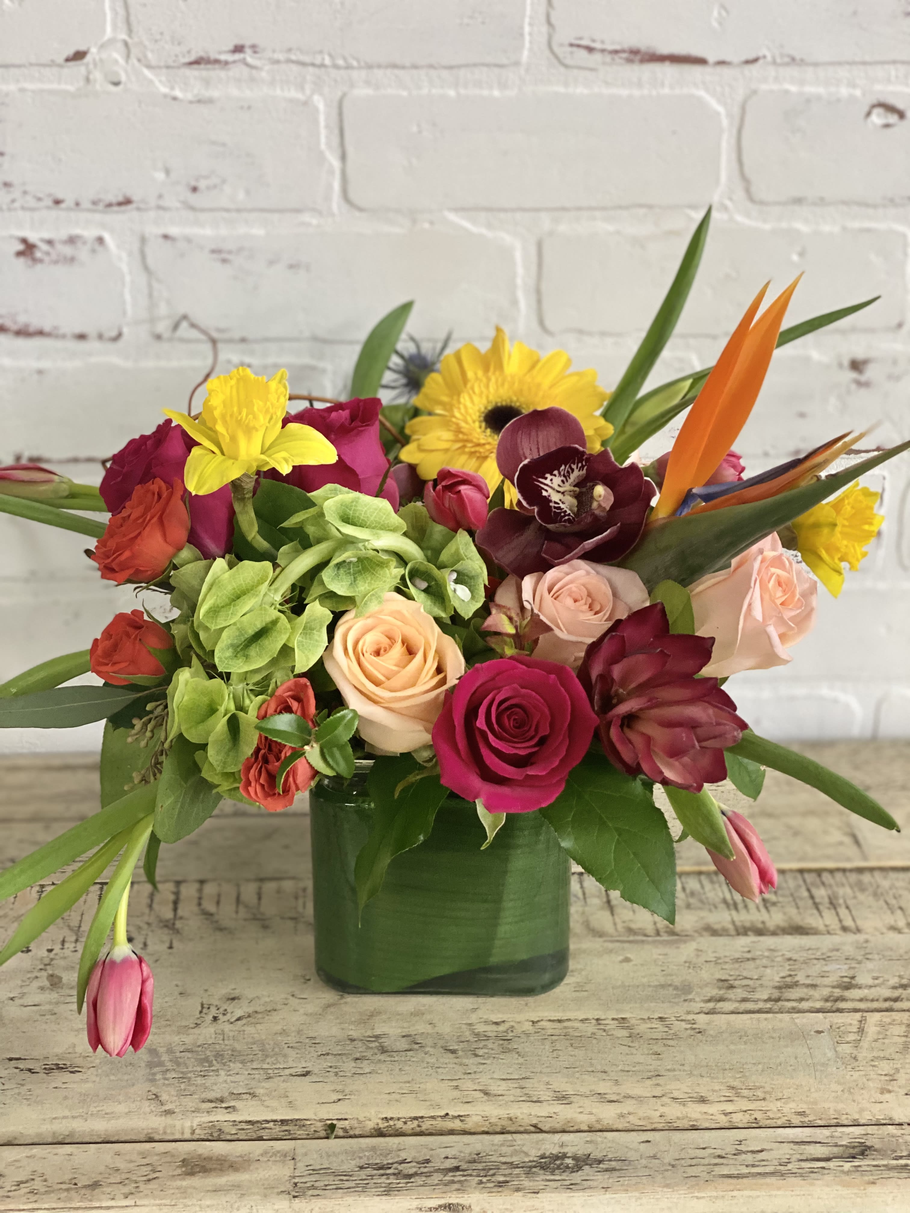 Mixed bouquet of roses, orchids, and bright tropical flowers in a green vase