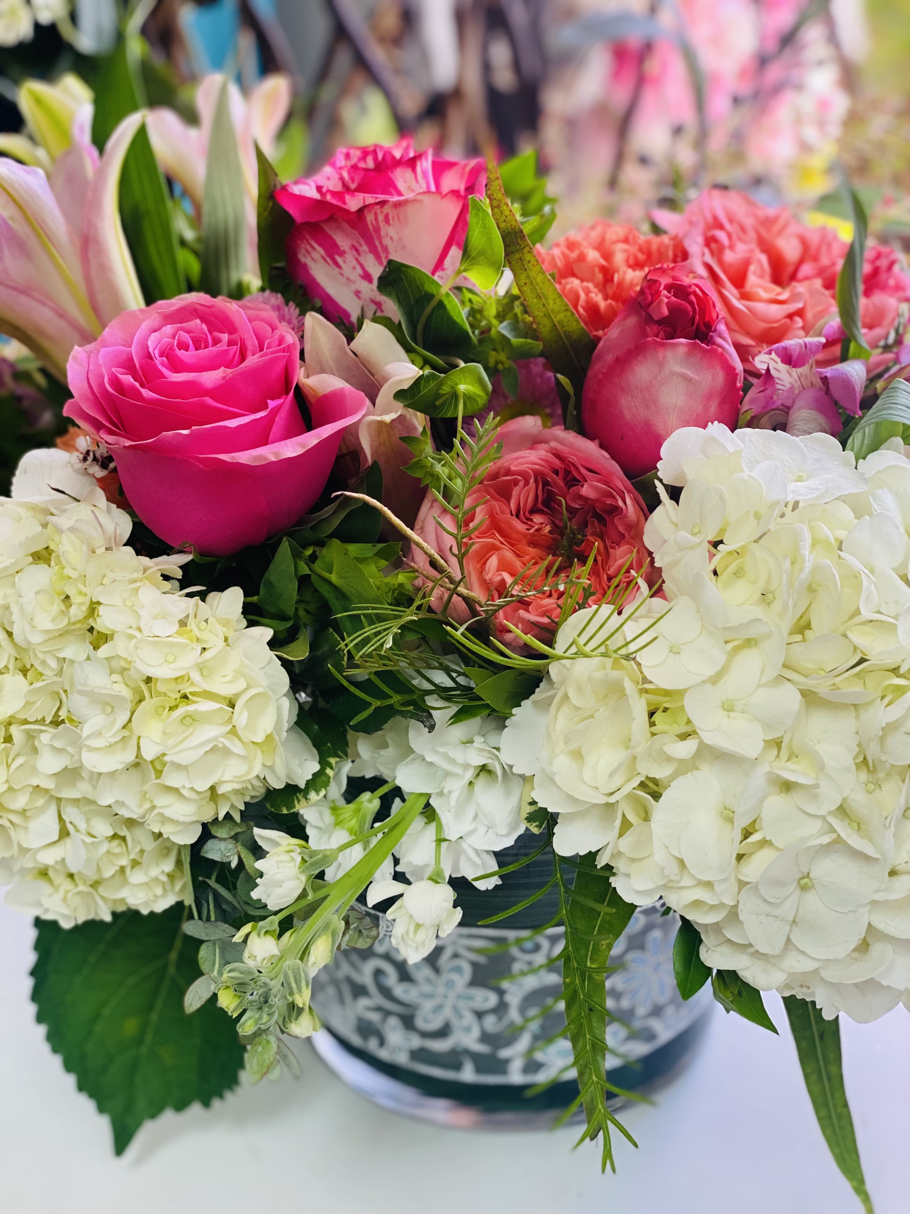 Low arrangement of bright pink roses, white hydrangeas, and coral blooms in a patterned container