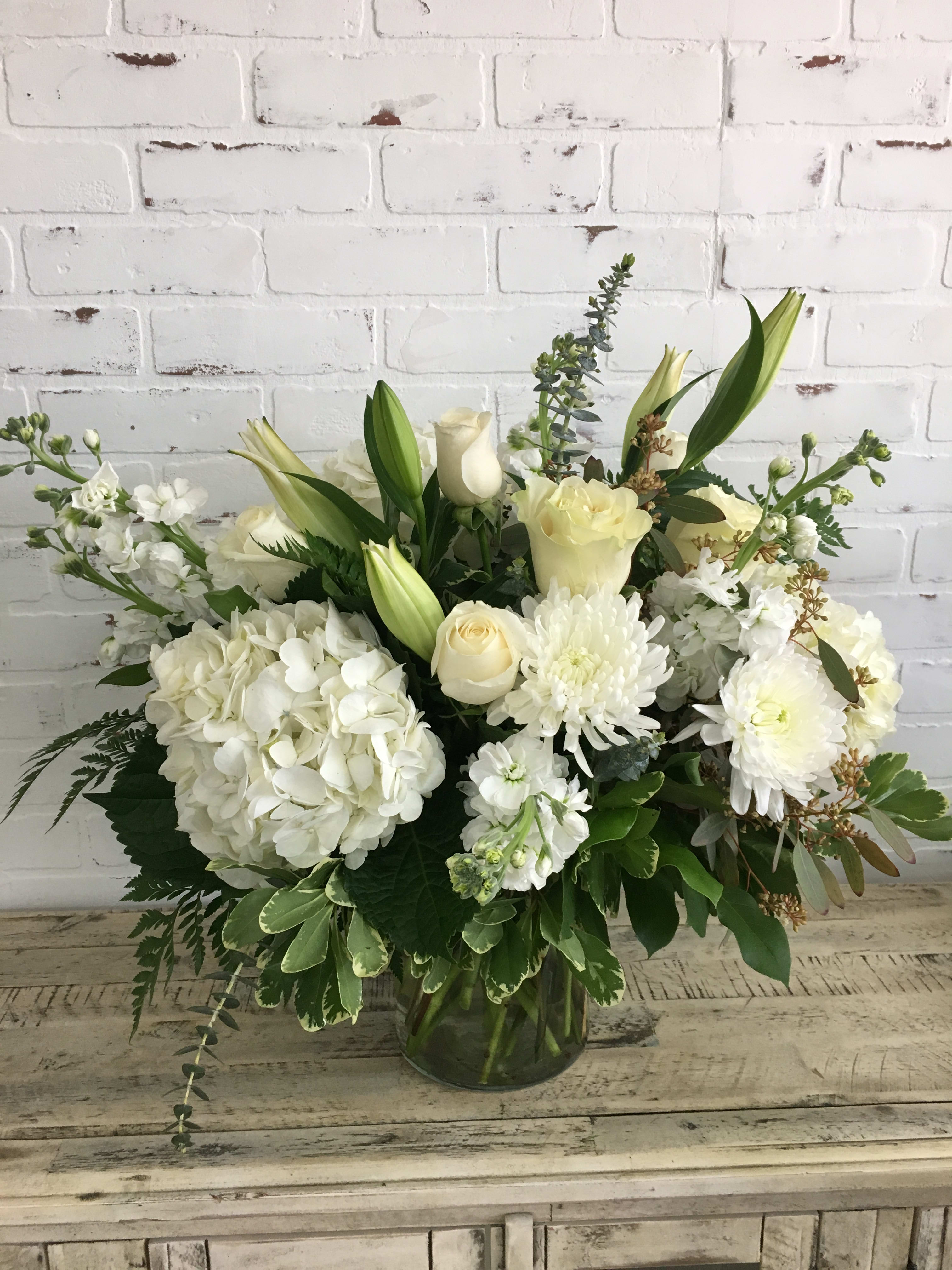 White hydrangeas, roses, lilies, and mums arranged in a clear glass vase