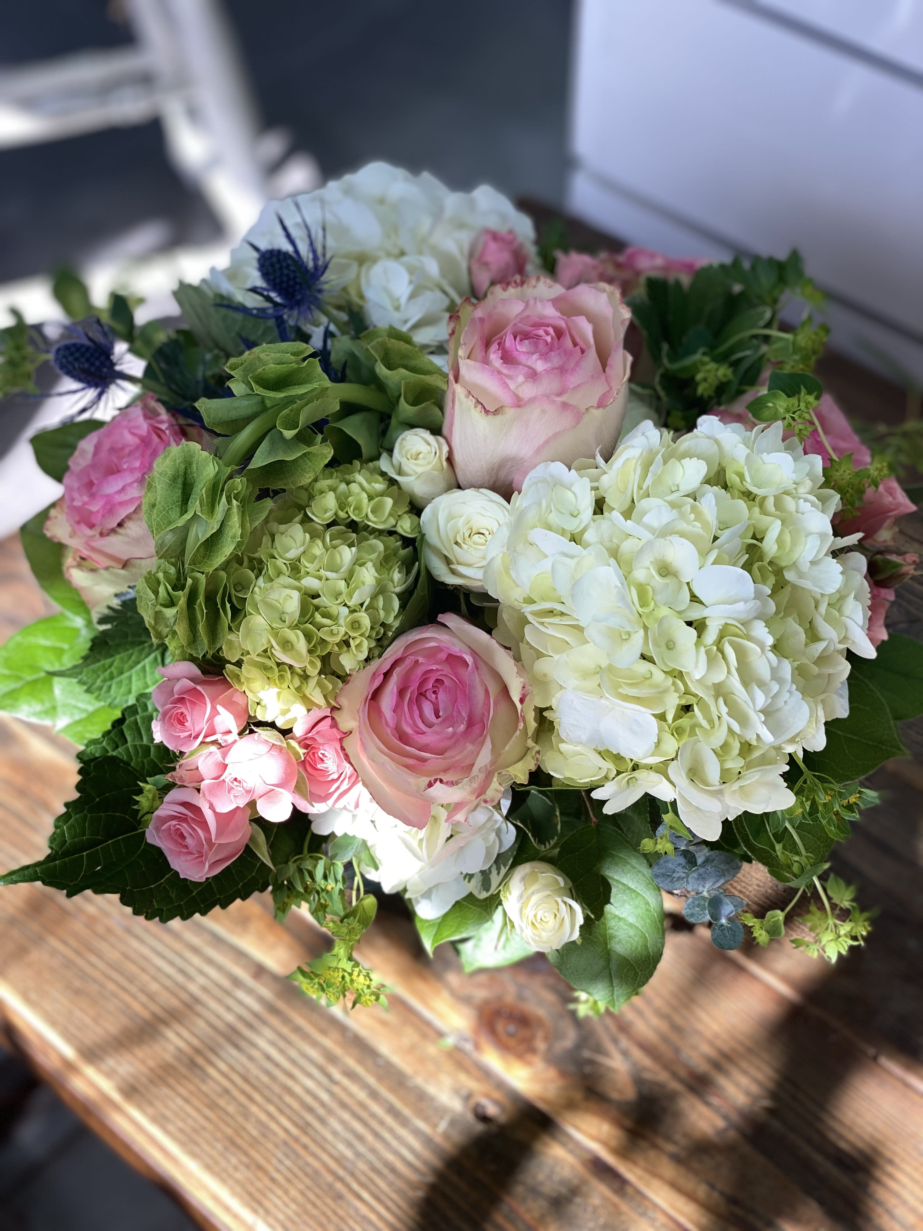 Round arrangement of pink roses with white and green hydrangeas in a low glass vase